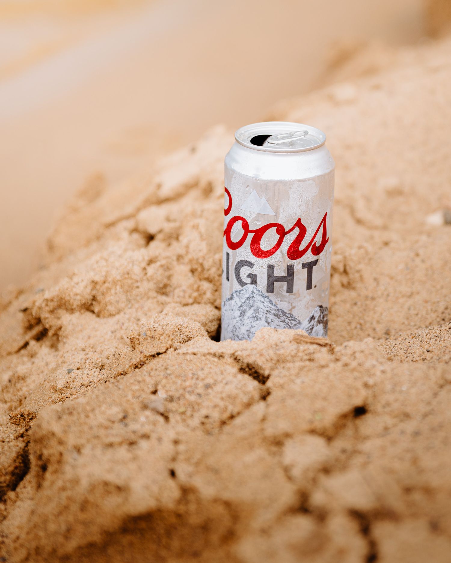 Beer cans buried in sand at varying depths show a progression of Coors Light being covered by beach sand.