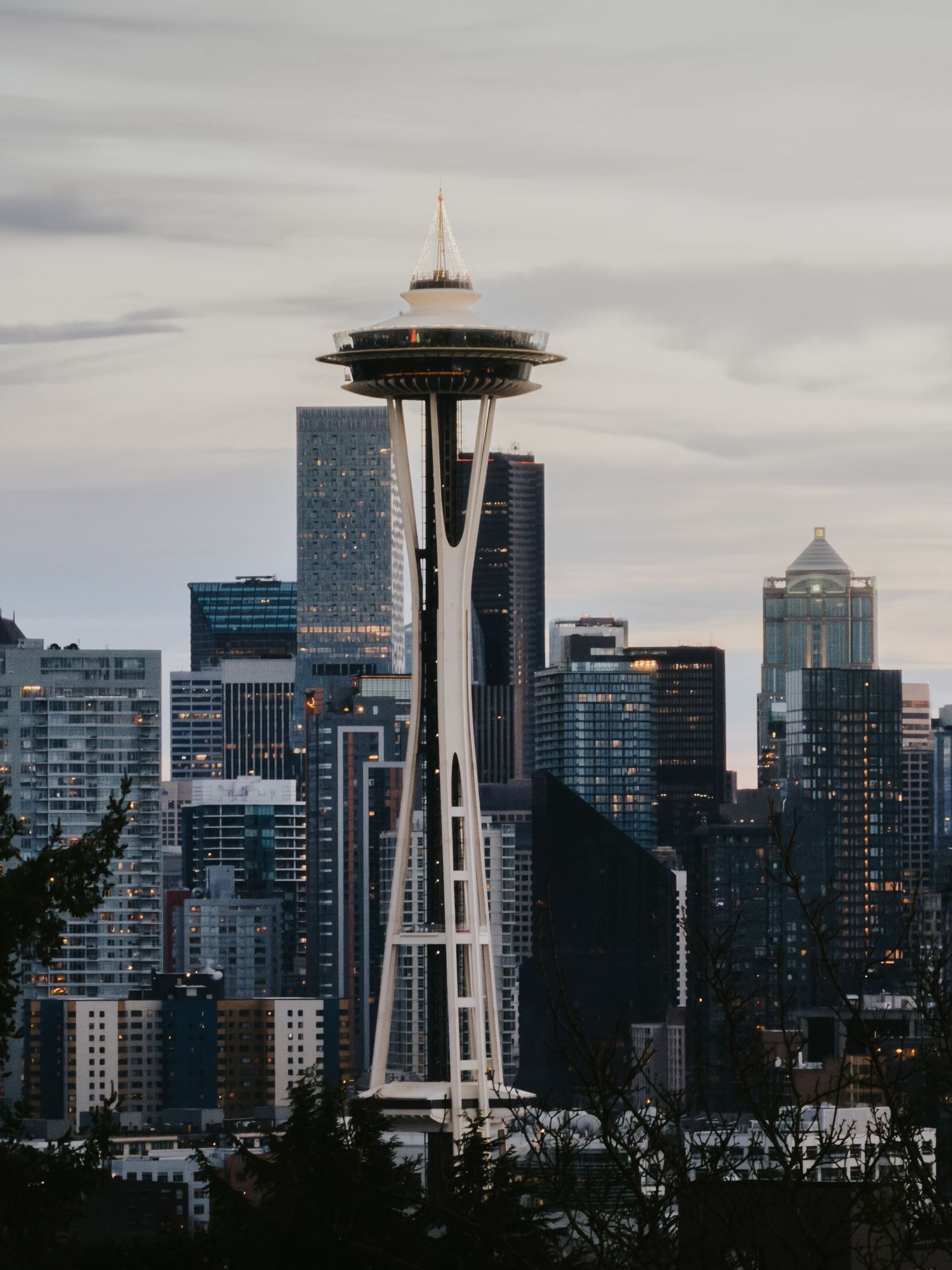 The iconic Space Needle towers over Seattle's downtown skyline against a cloudy evening sky.