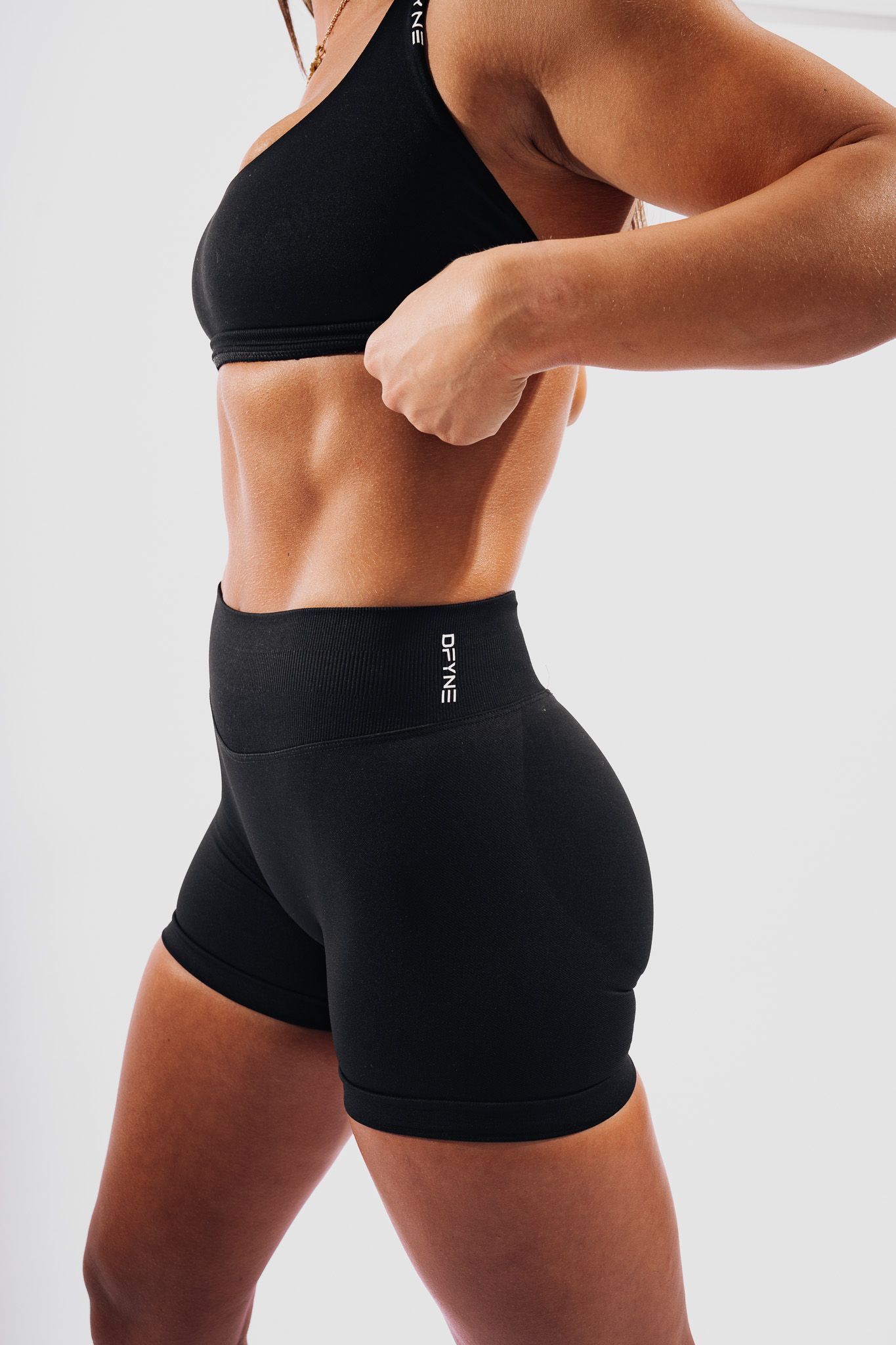 Athletic figure wearing black sports bra and high-waisted compression shorts showing fit physique against white background.