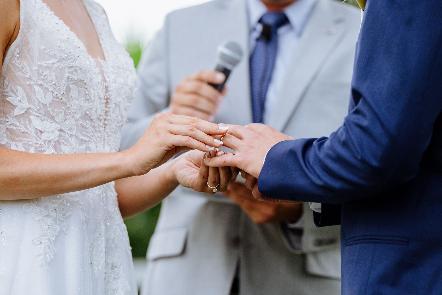 A close-up of hands exchanging wedding rings during an outdoor ceremony.