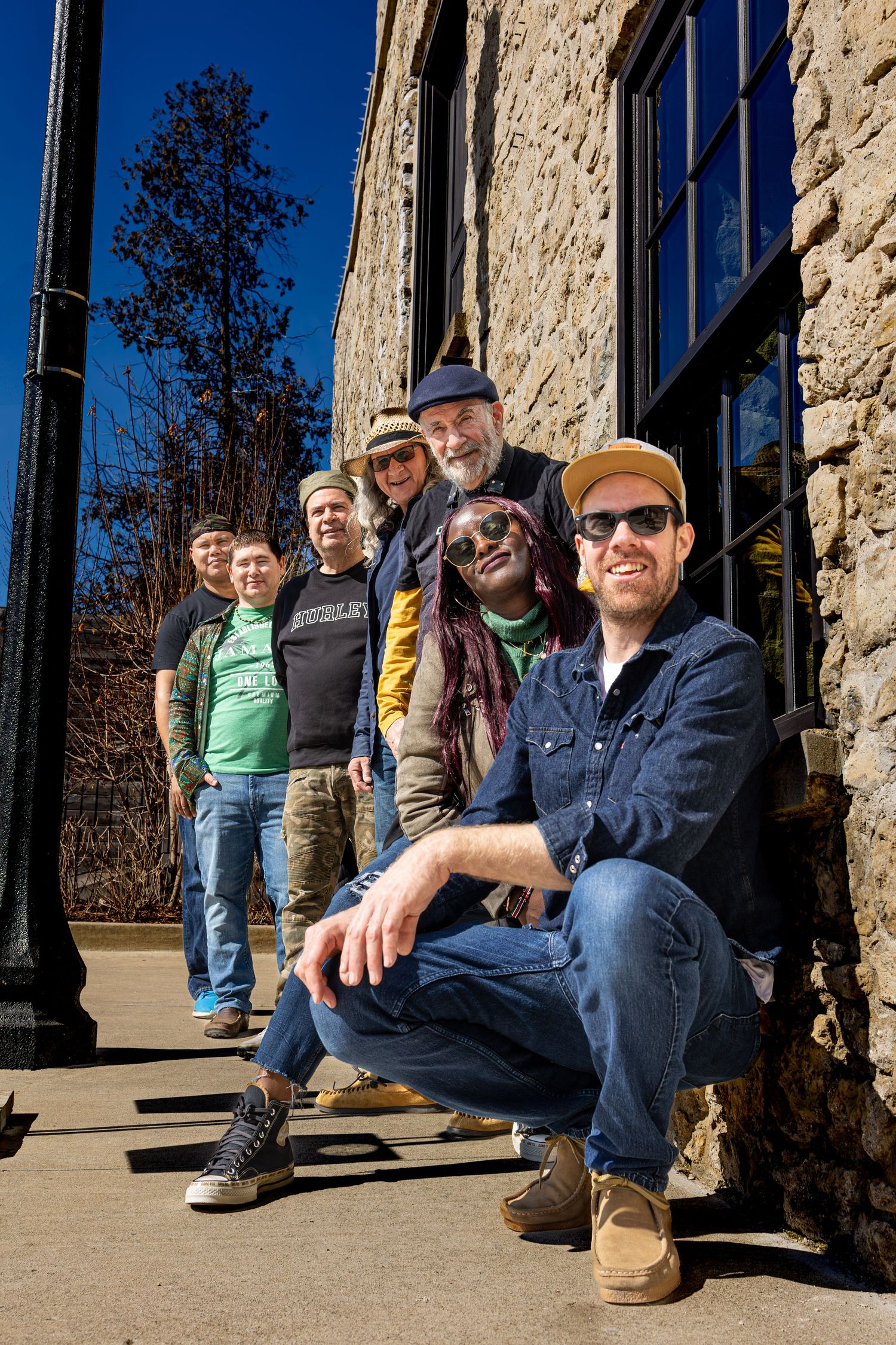Group of musicians sitting casually on outdoor stone steps on a sunny day.