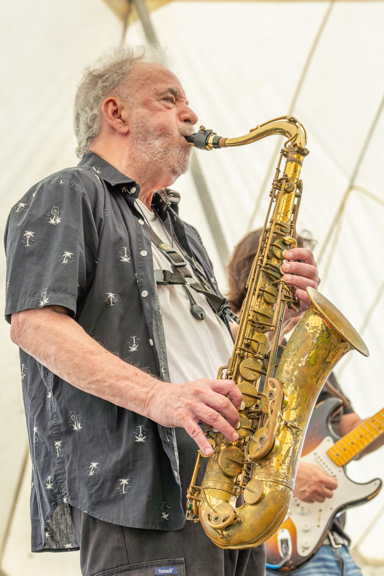 Jazz musician performs on saxophone wearing dark button-up shirt with anchor pattern during outdoor concert performance.