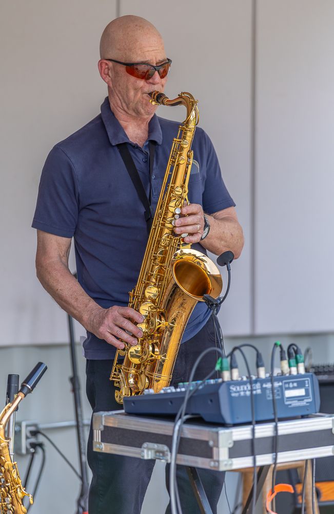 Saxophonist in navy blue shirt performs on stage with electronic keyboard equipment in background.
