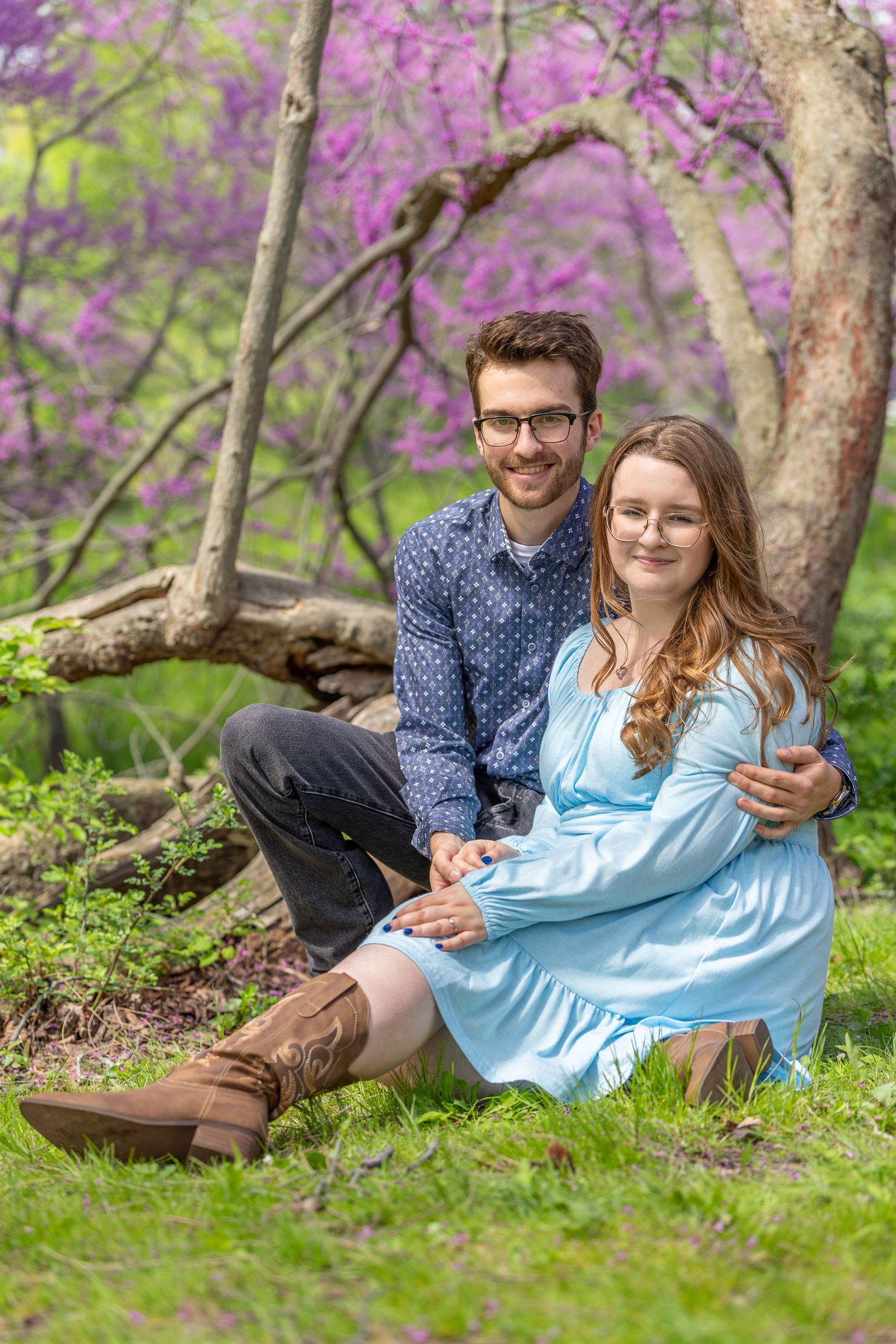 A couple relaxes together under blooming spring trees with purple flowers in a romantic outdoor setting.