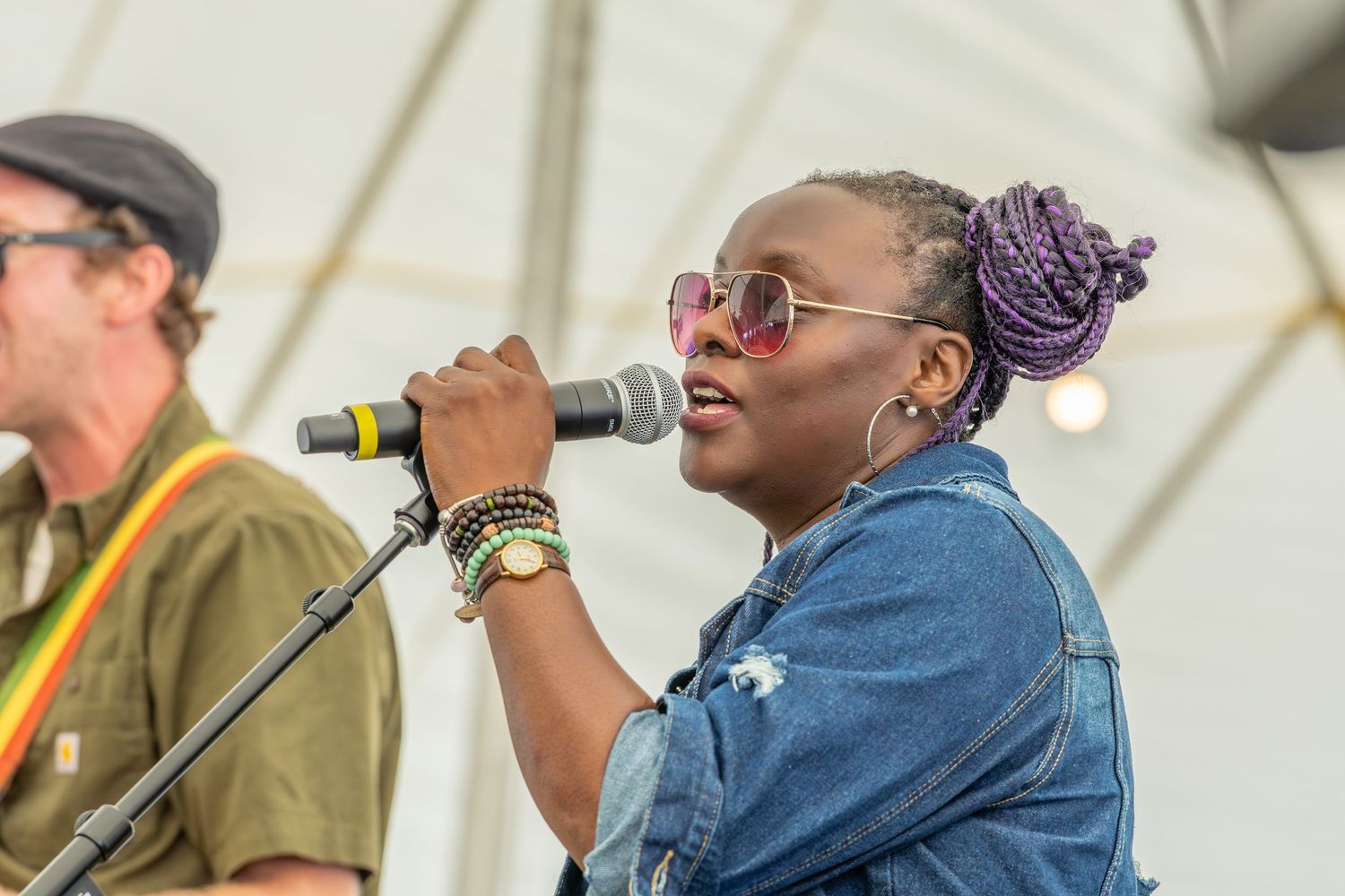 Musicians perform together on stage during an outdoor festival concert with instruments and microphones.