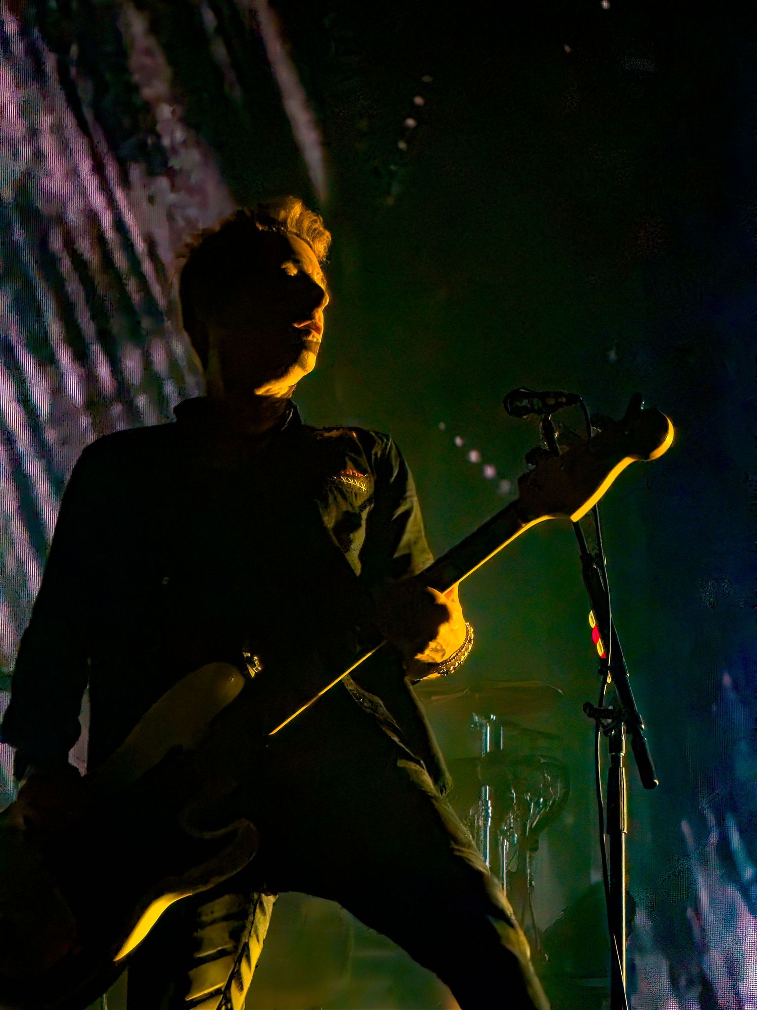Silhouetted performer on stage illuminated by dramatic yellow lighting creates moody atmosphere during concert performance.