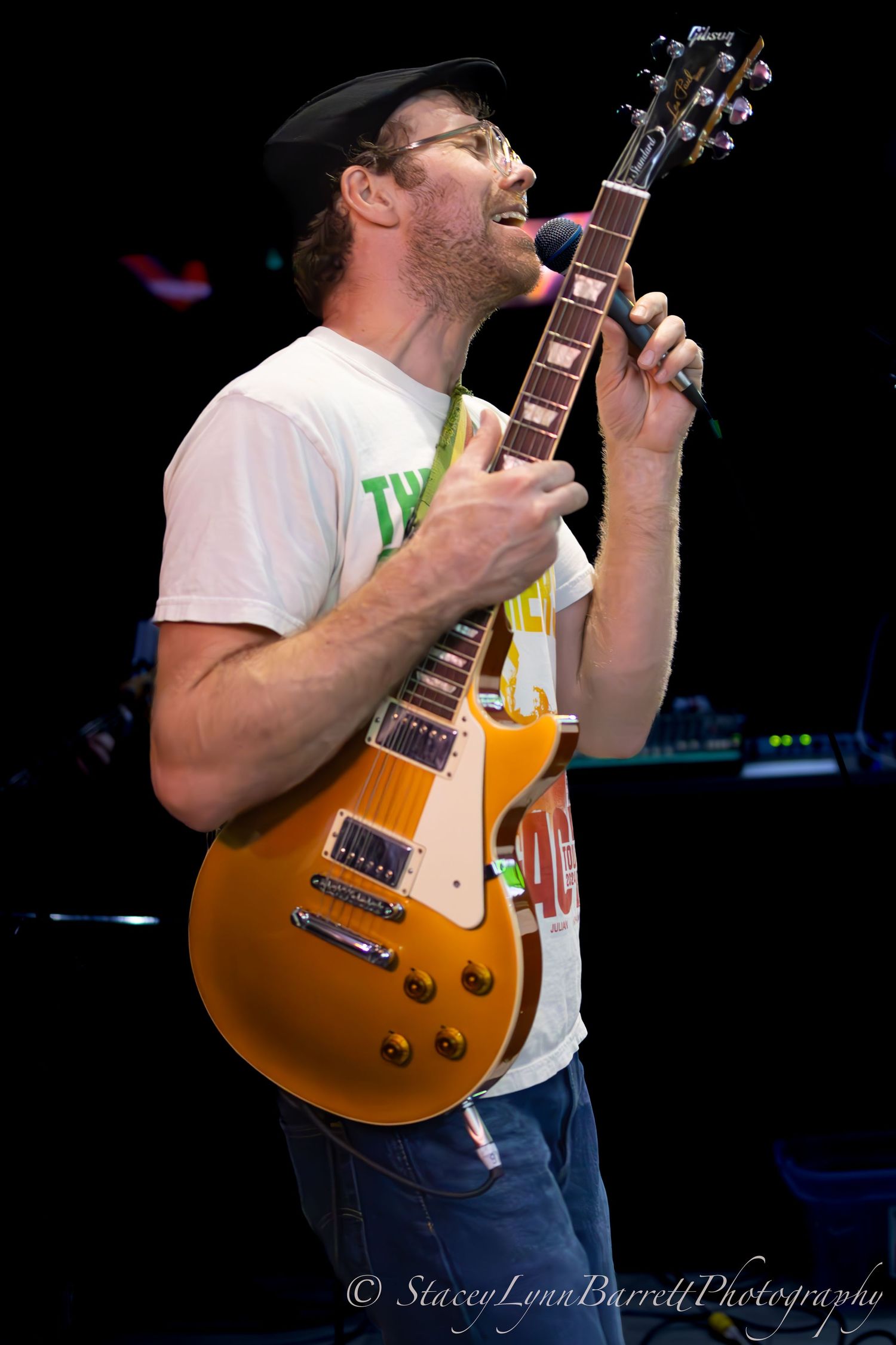 A musician playing a honey-colored Gibson Les Paul guitar on stage.