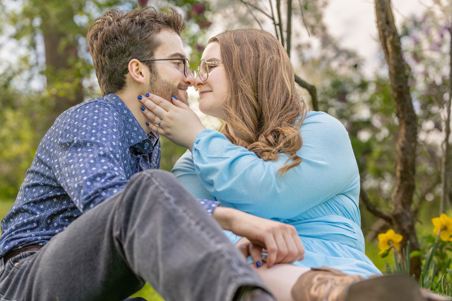 A couple sharing a tender kiss outdoors in a natural setting with flowers and greenery in the background.