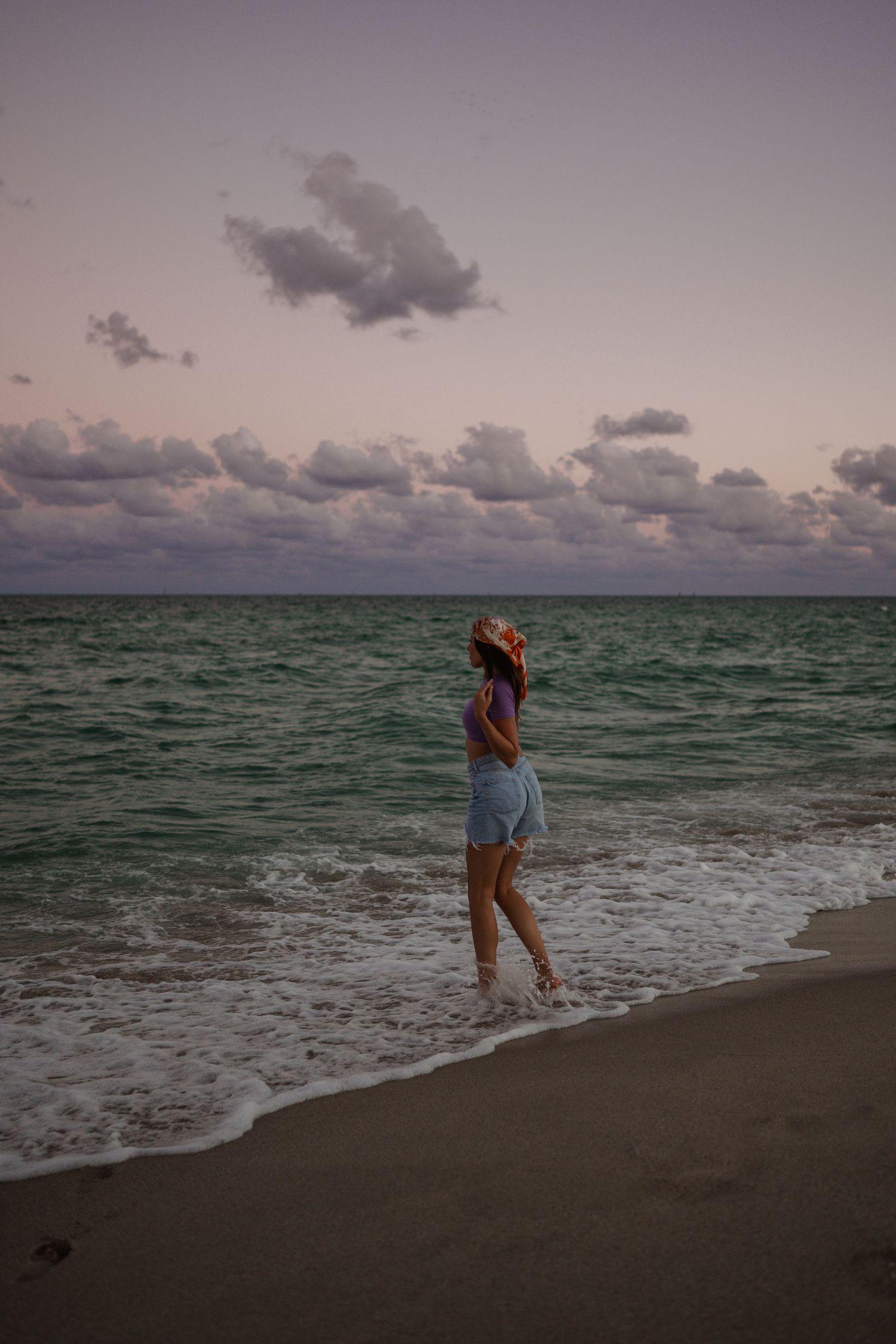 A silhouette stands on a beach during sunset with dark clouds looming over the turquoise ocean waters.