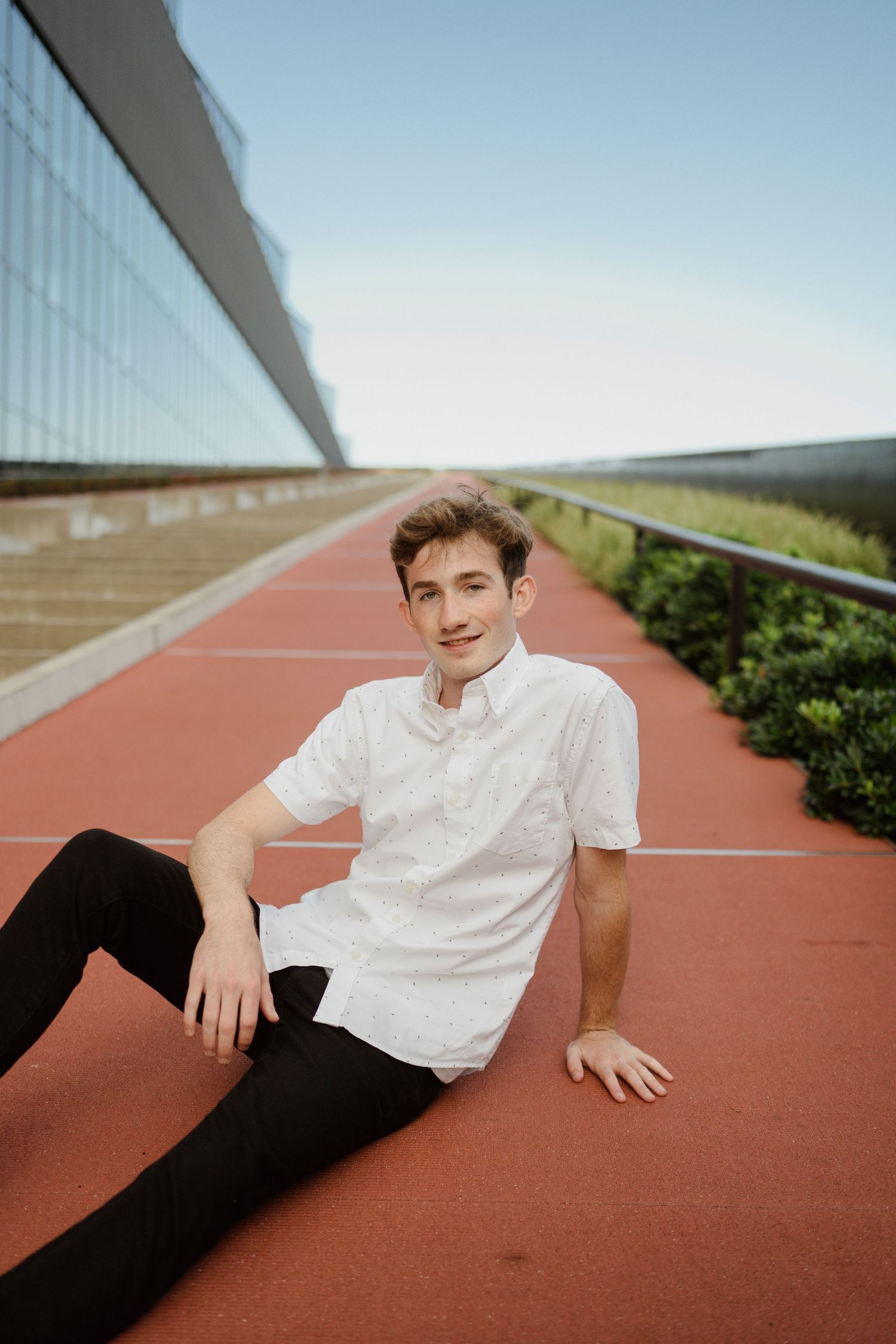 Person relaxing on red running track wearing white shirt and black pants.