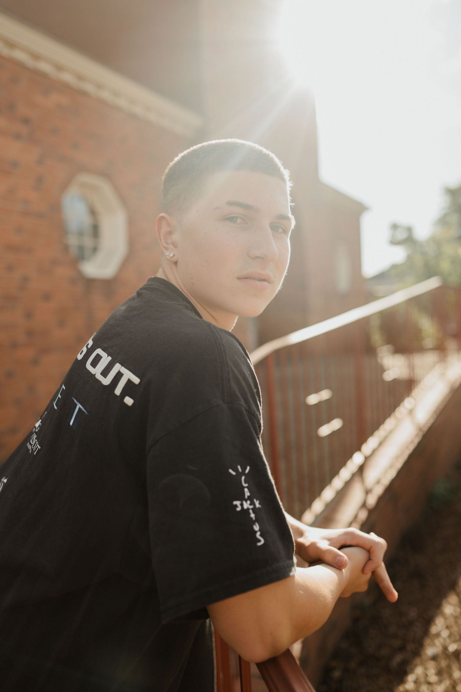 Side profile portrait of someone in a black t-shirt standing against a brick wall in golden sunlight.