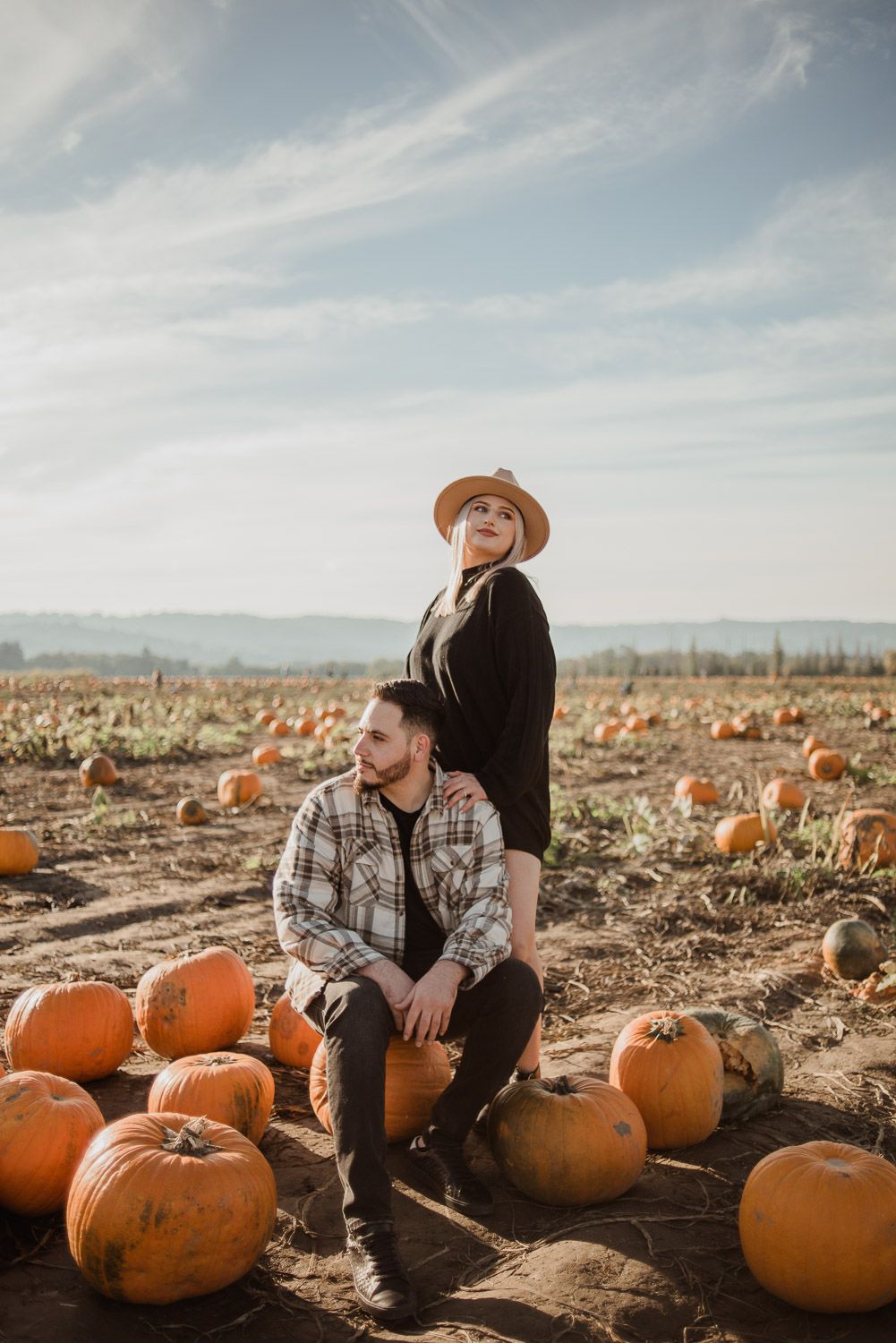 A couple poses in a pumpkin patch field during golden hour wearing western-inspired outfits.
