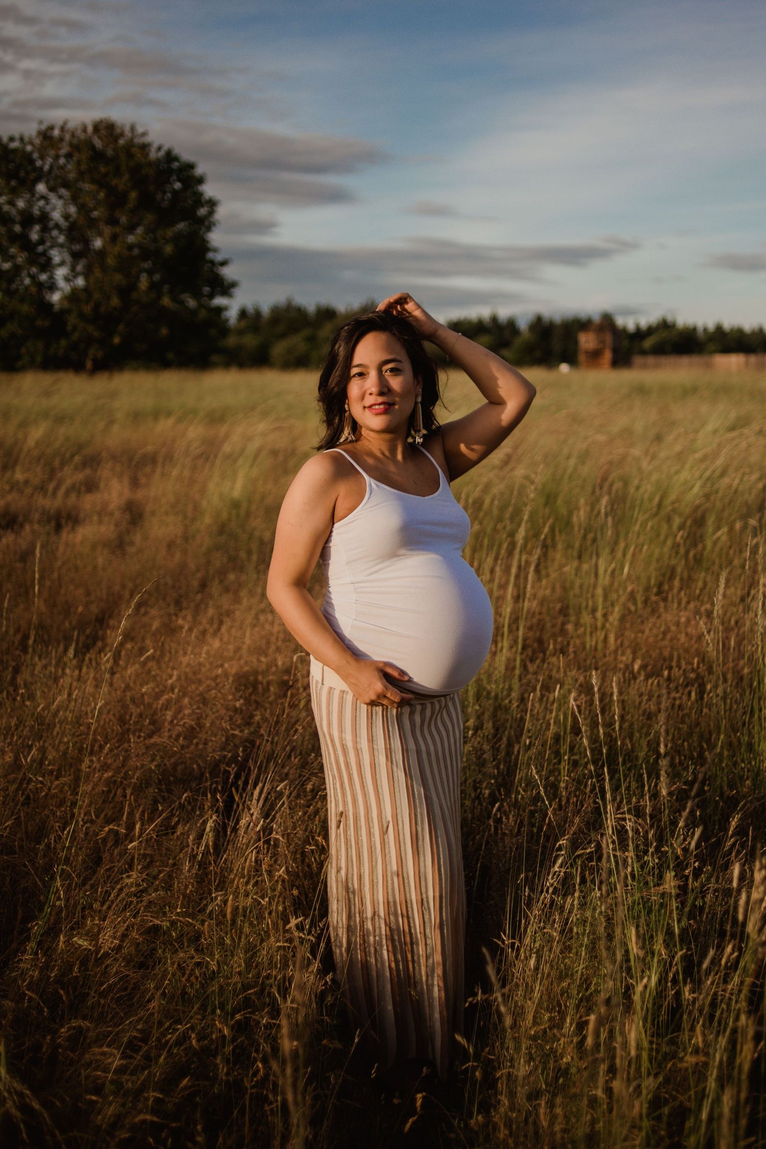 A maternity photo taken in a golden field at sunset with warm lighting and tall grass.