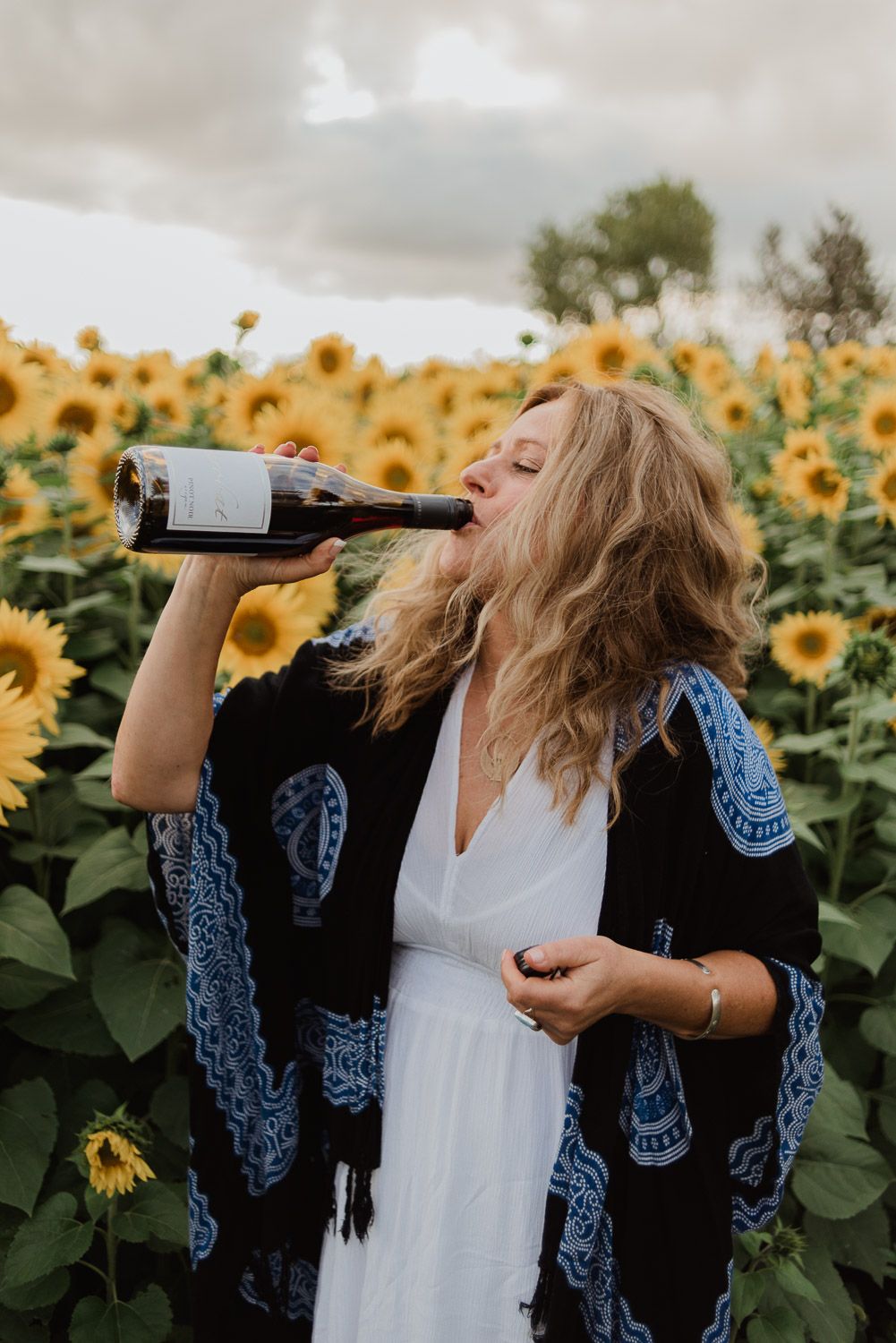 Carefree moment drinking wine in sunflower field wearing blue patterned kimono.