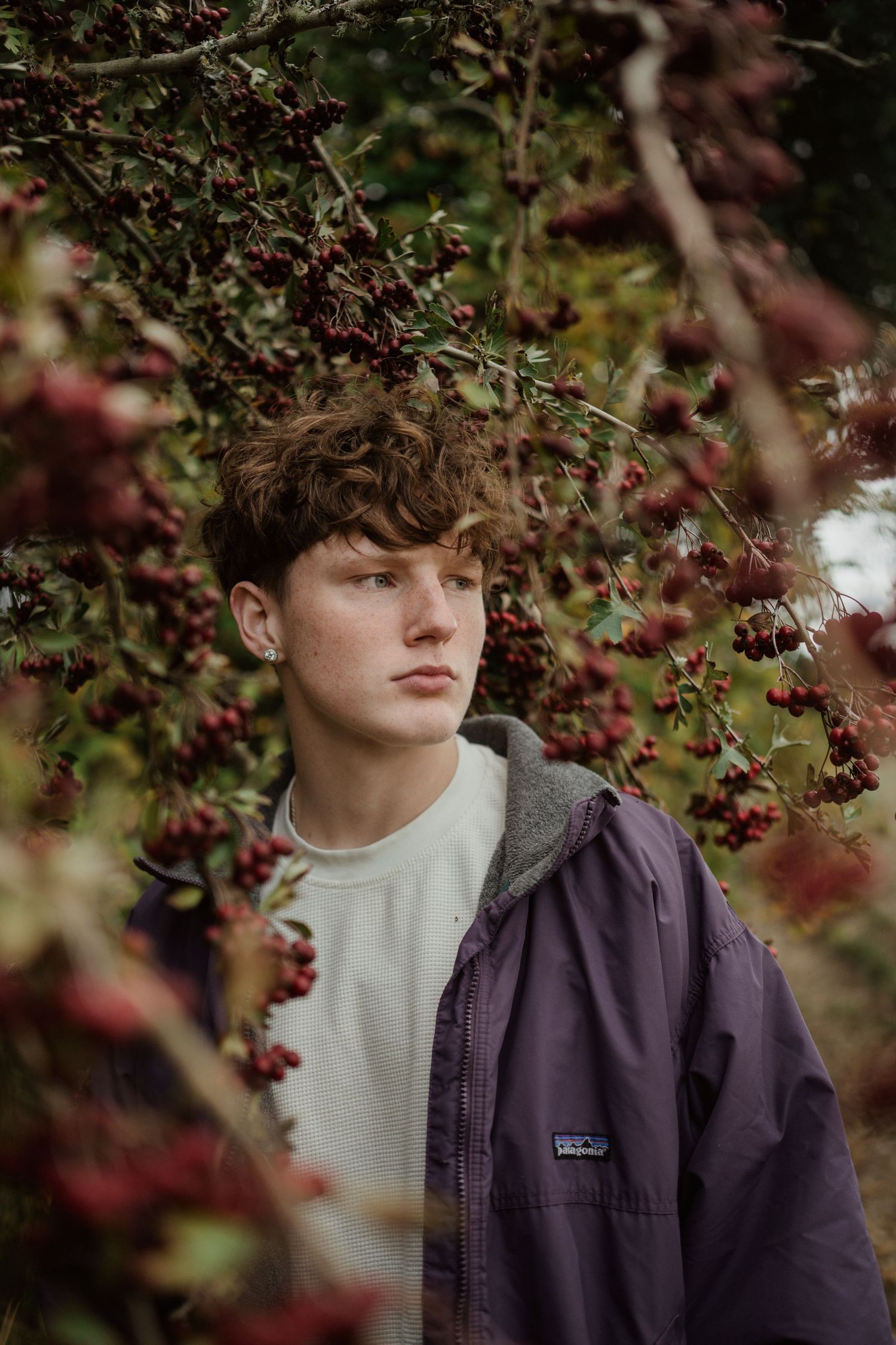 A portrait amongst autumn berry branches wearing a purple jacket and cream sweater.