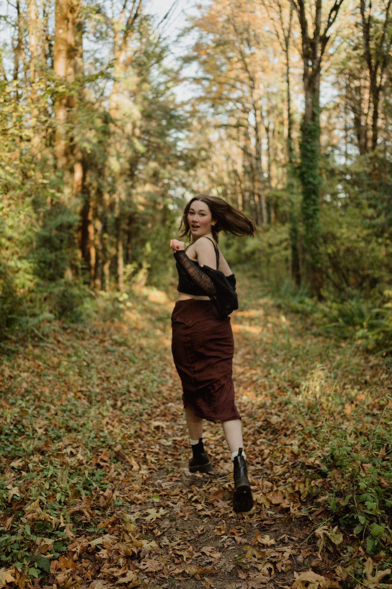 Dynamic autumn fashion photo of figure twirling in burgundy skirt on forest path.