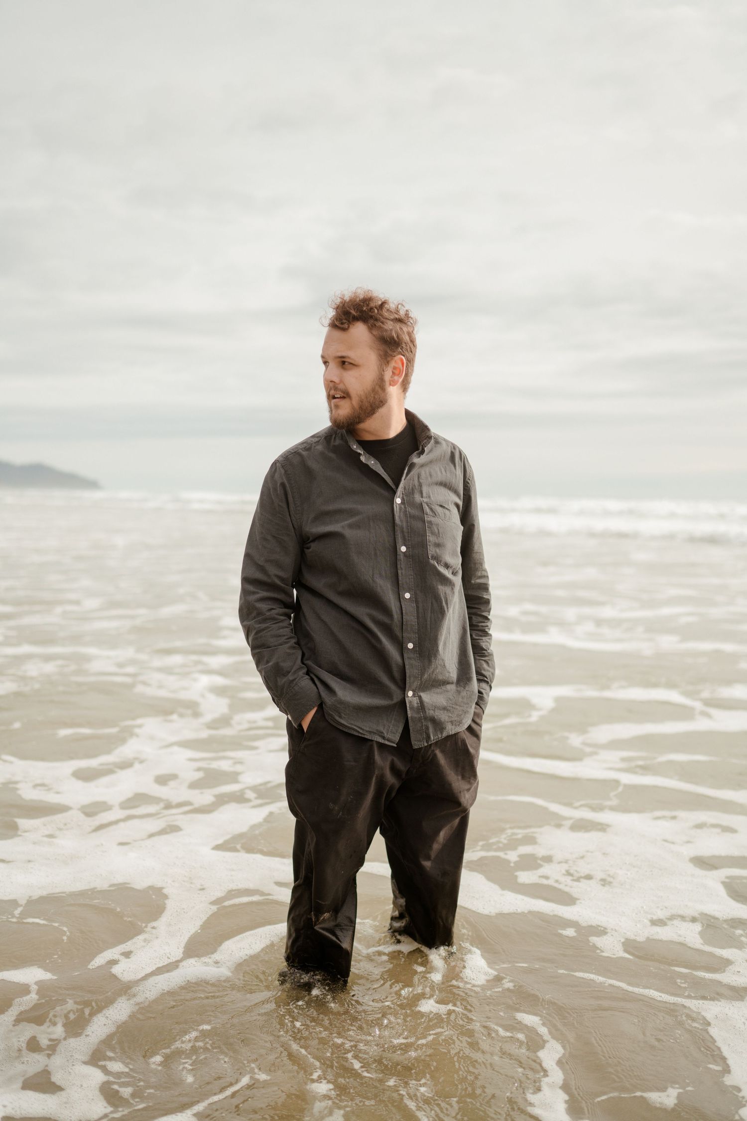 Person in casual grey jacket standing in ocean surf.