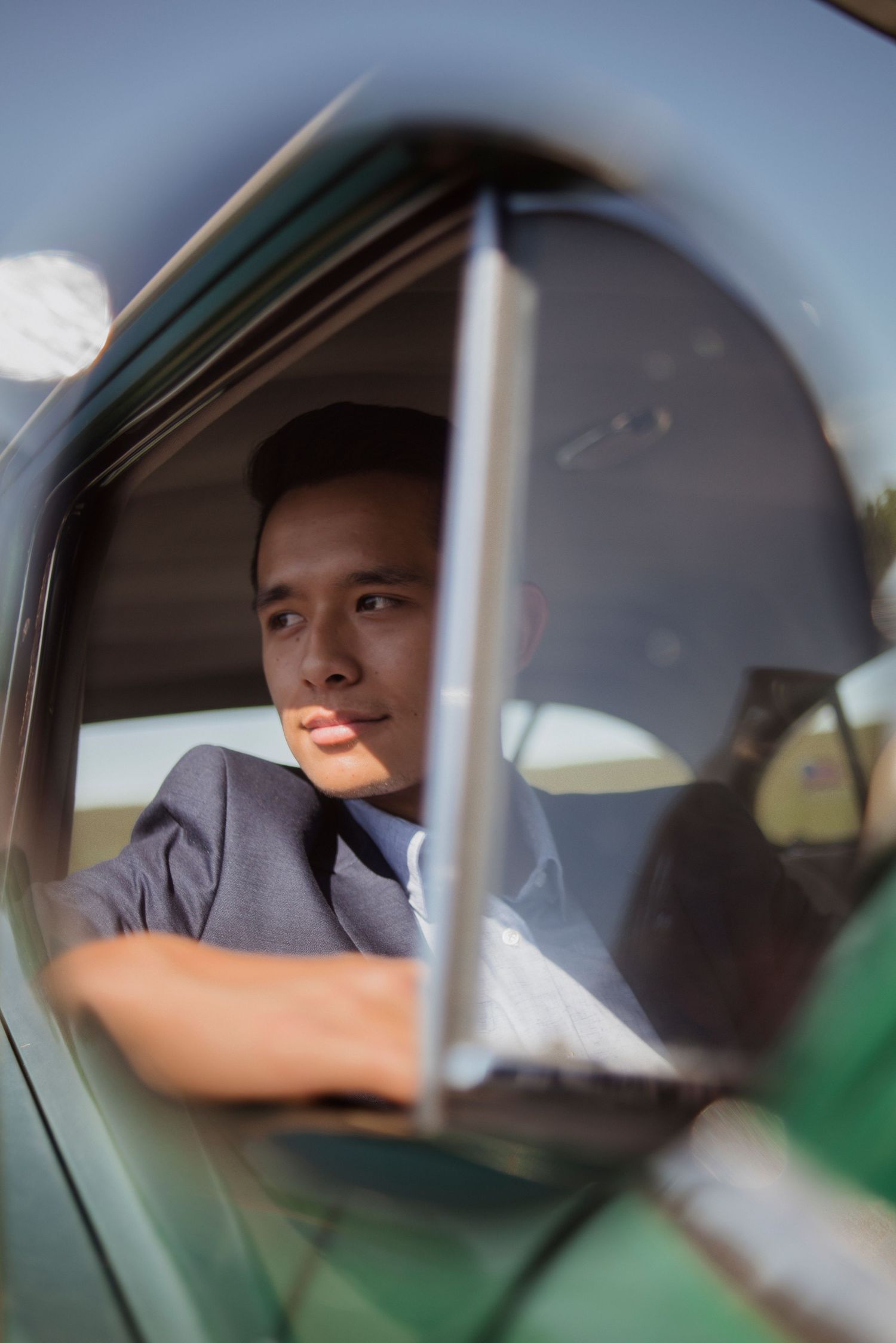 Portrait through car window showing navy-suited figure in warm sunlight.
