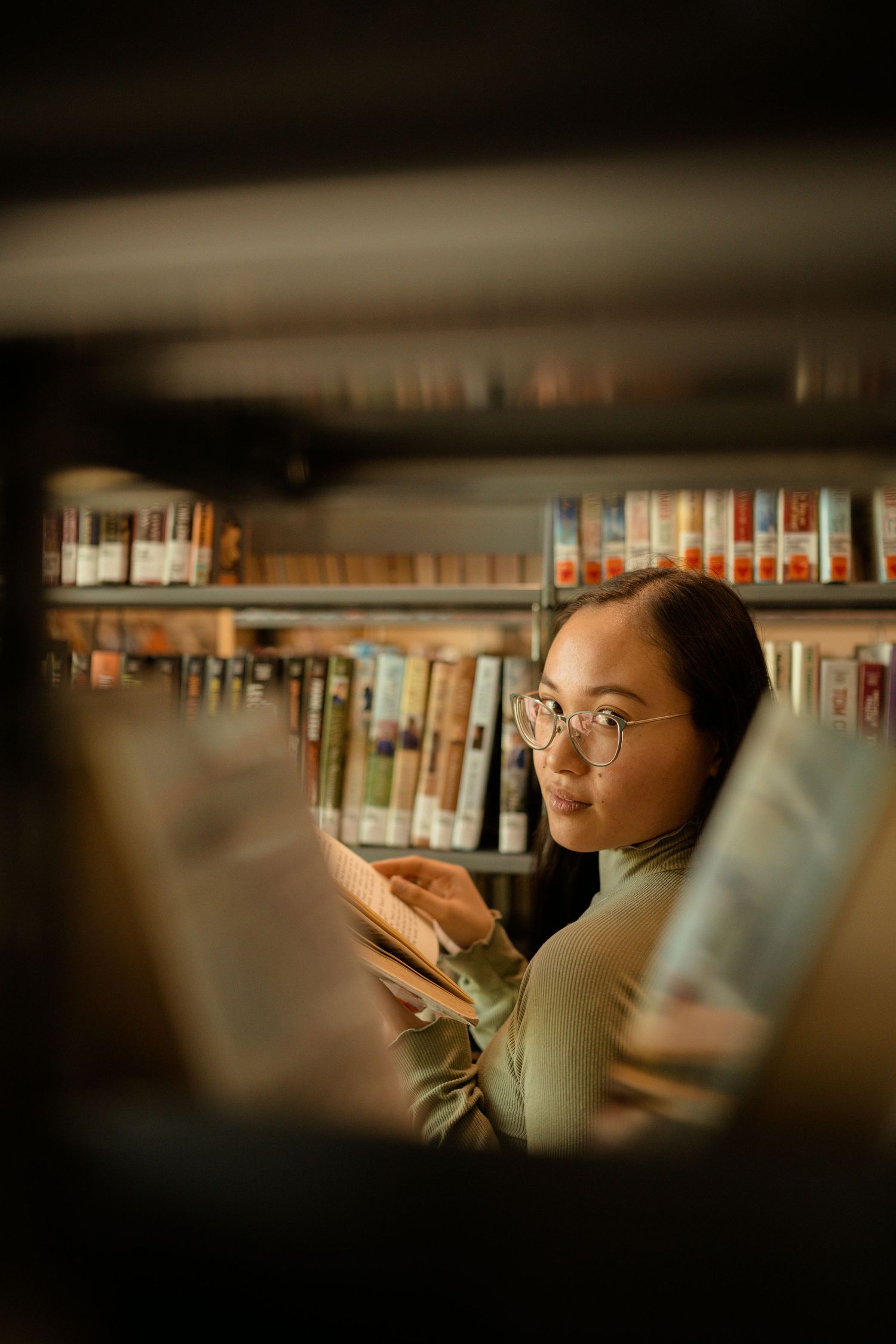 Reader browsing books between library shelves in warm lighting.