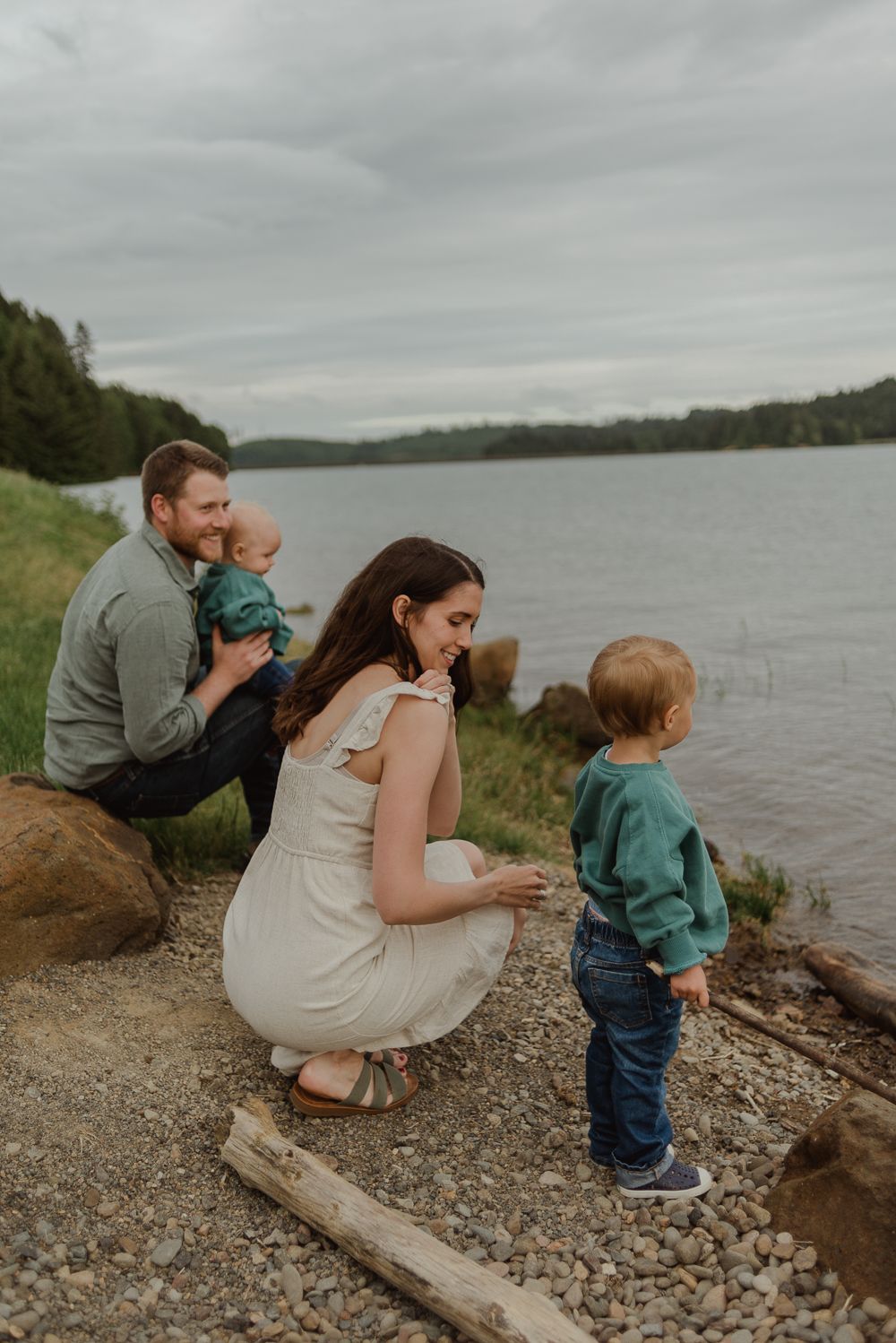 Family spending time together by rocky lakeshore on cloudy afternoon.