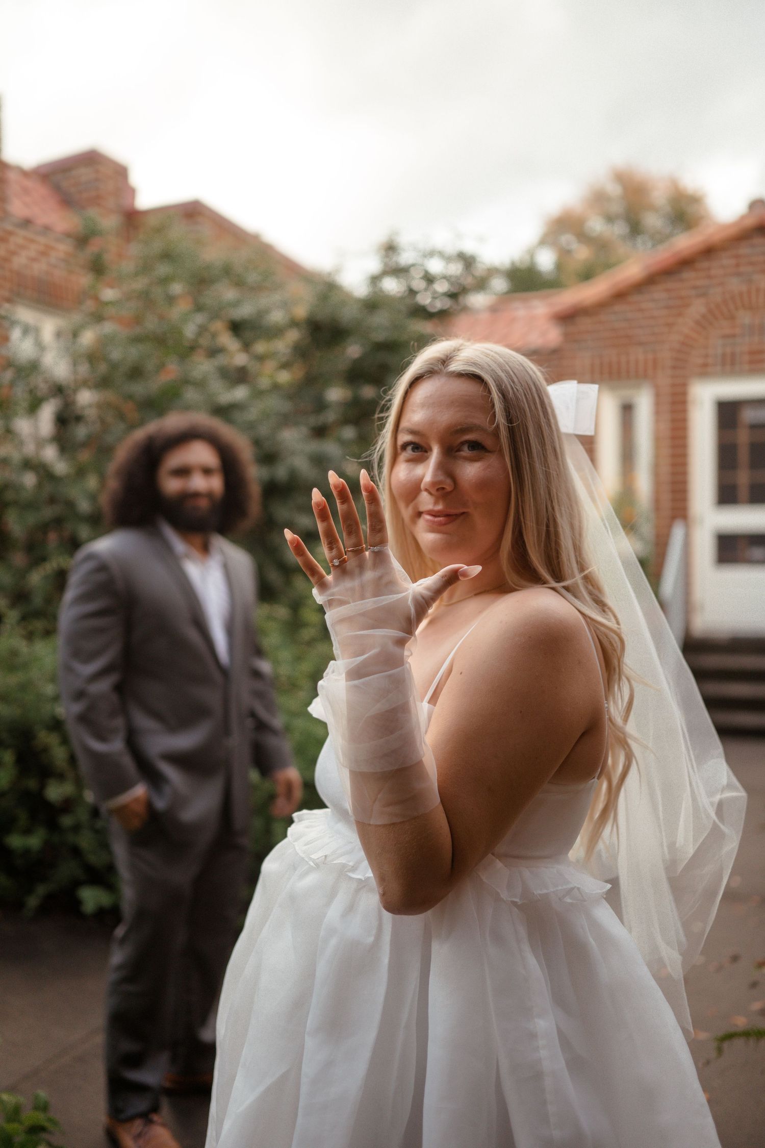 A bride shows off her ring while posing in a garden setting.
