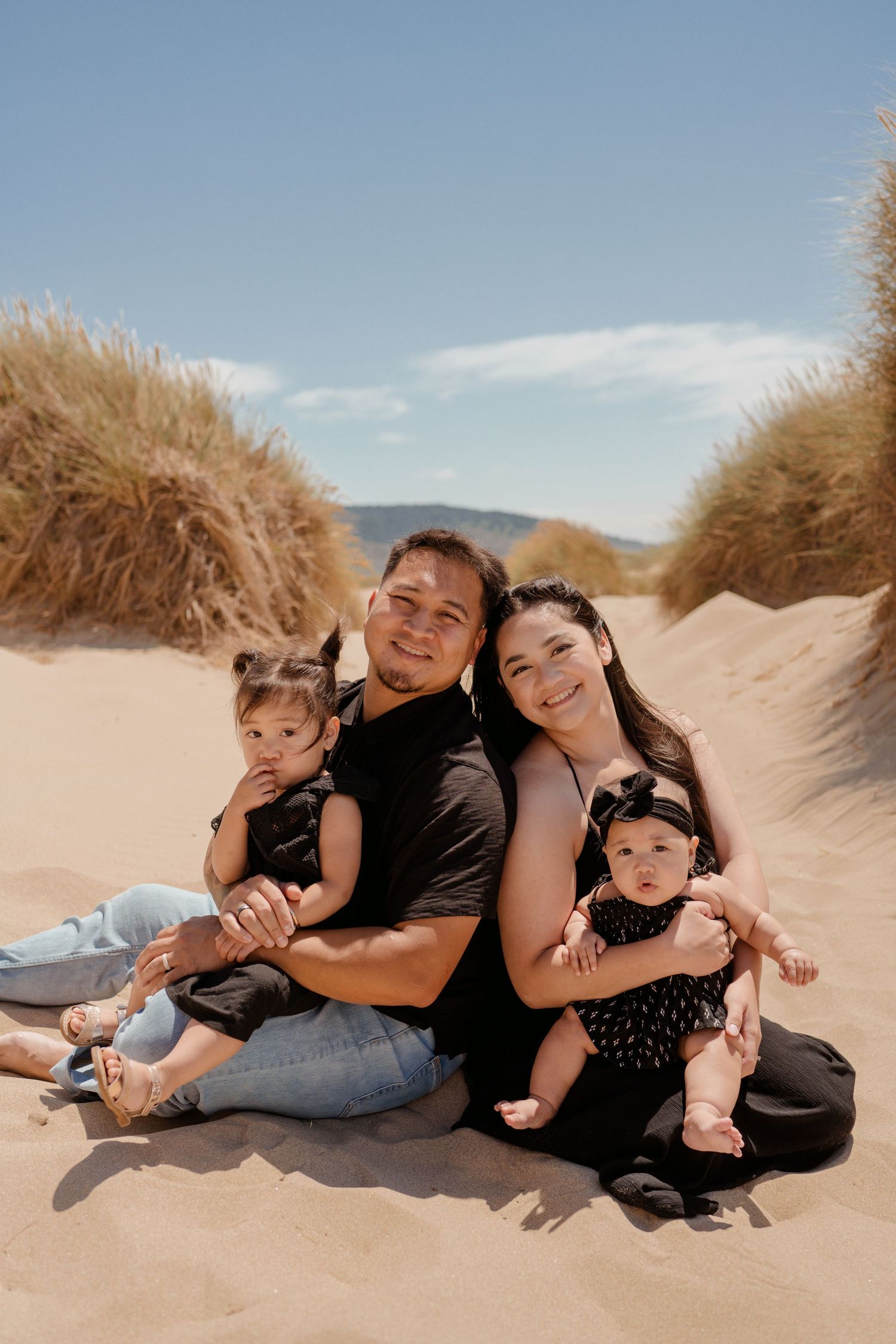 Family sitting together on sandy dunes under bright blue sky.