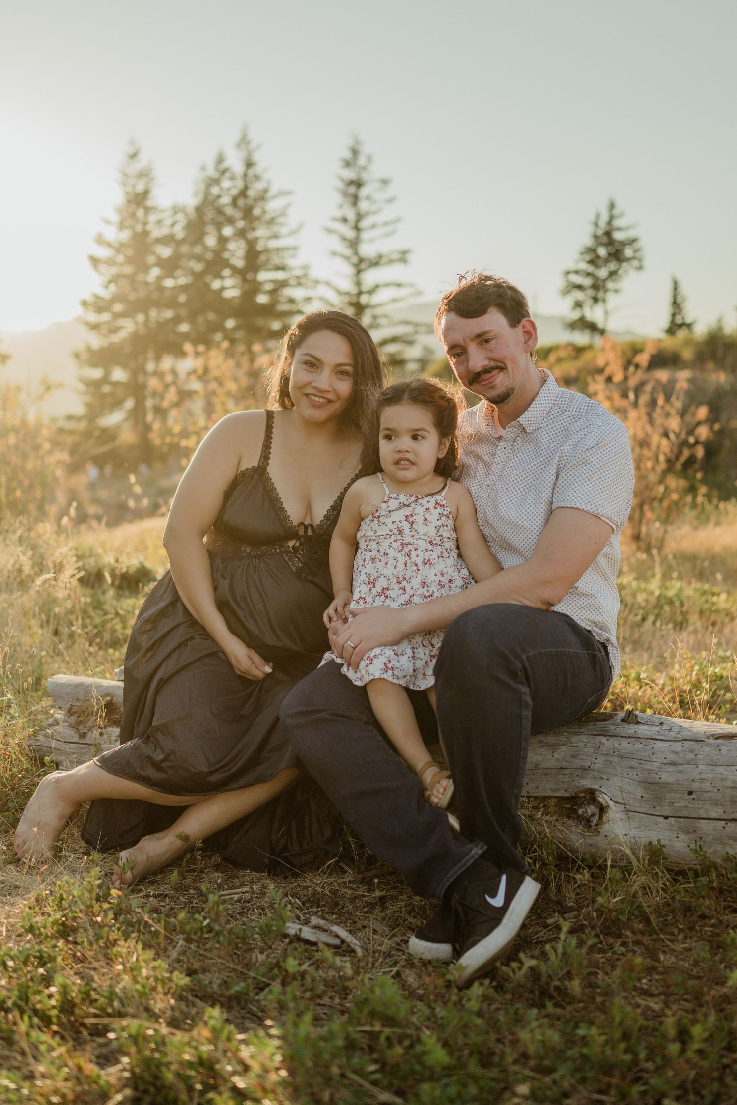 Family sitting on log during golden hour with mountain scenery behind them.