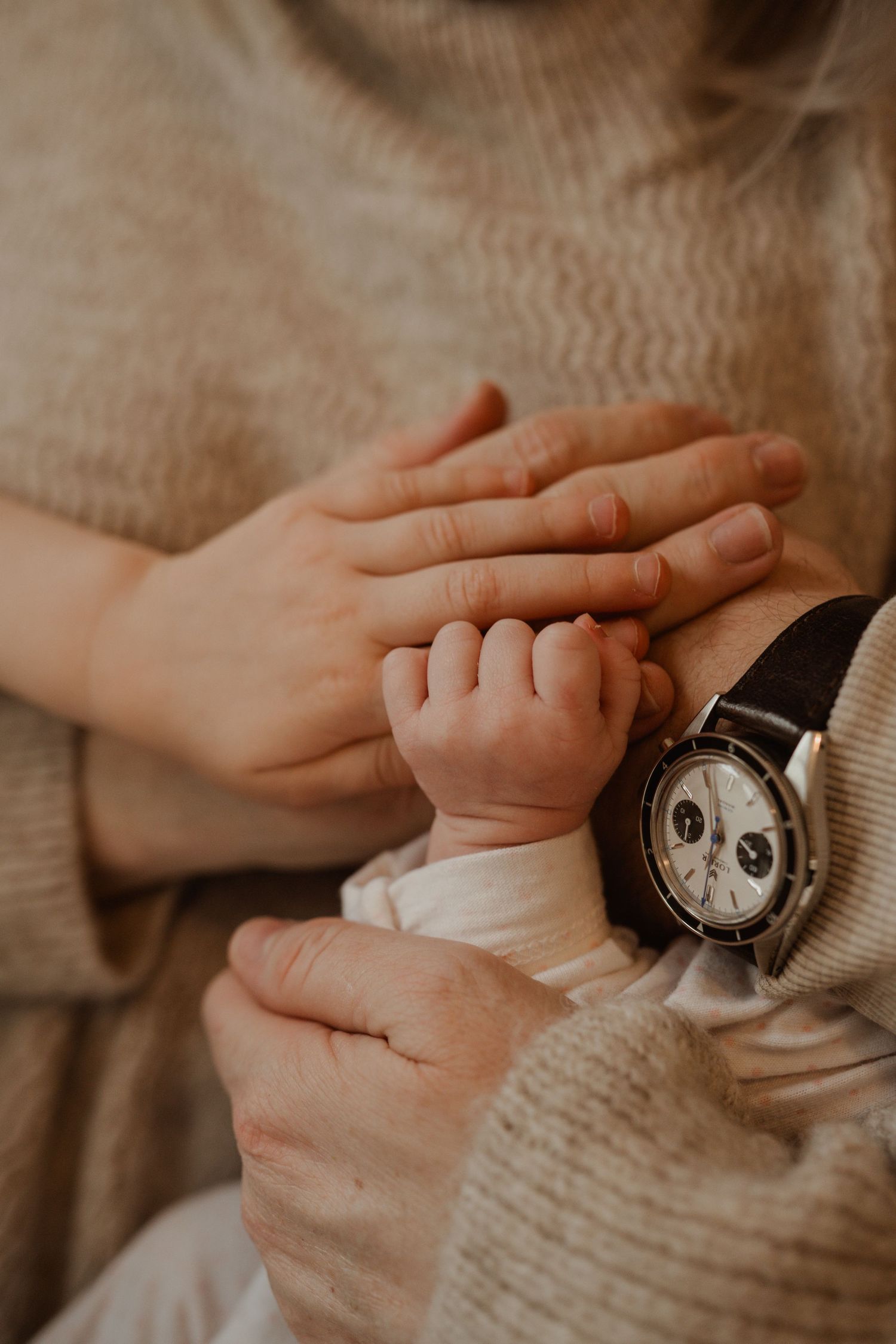 Close up of tiny baby hand touching parent's hands and wristwatch.