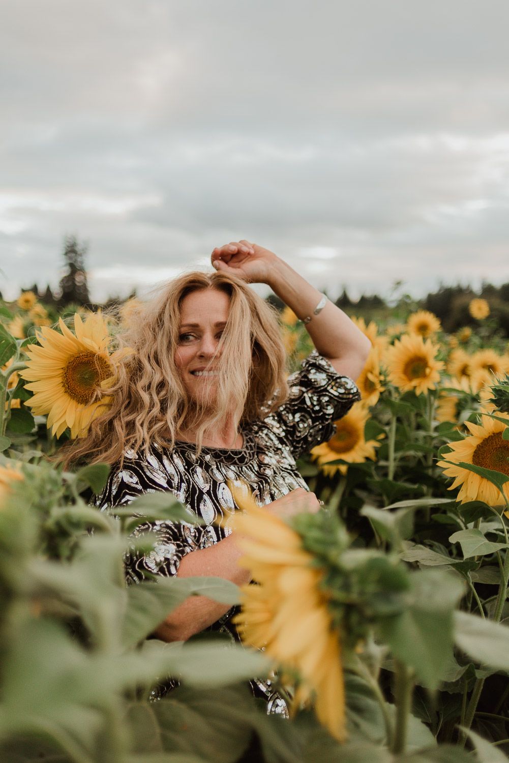 Joyful pose among blooming sunflowers on cloudy summer day.