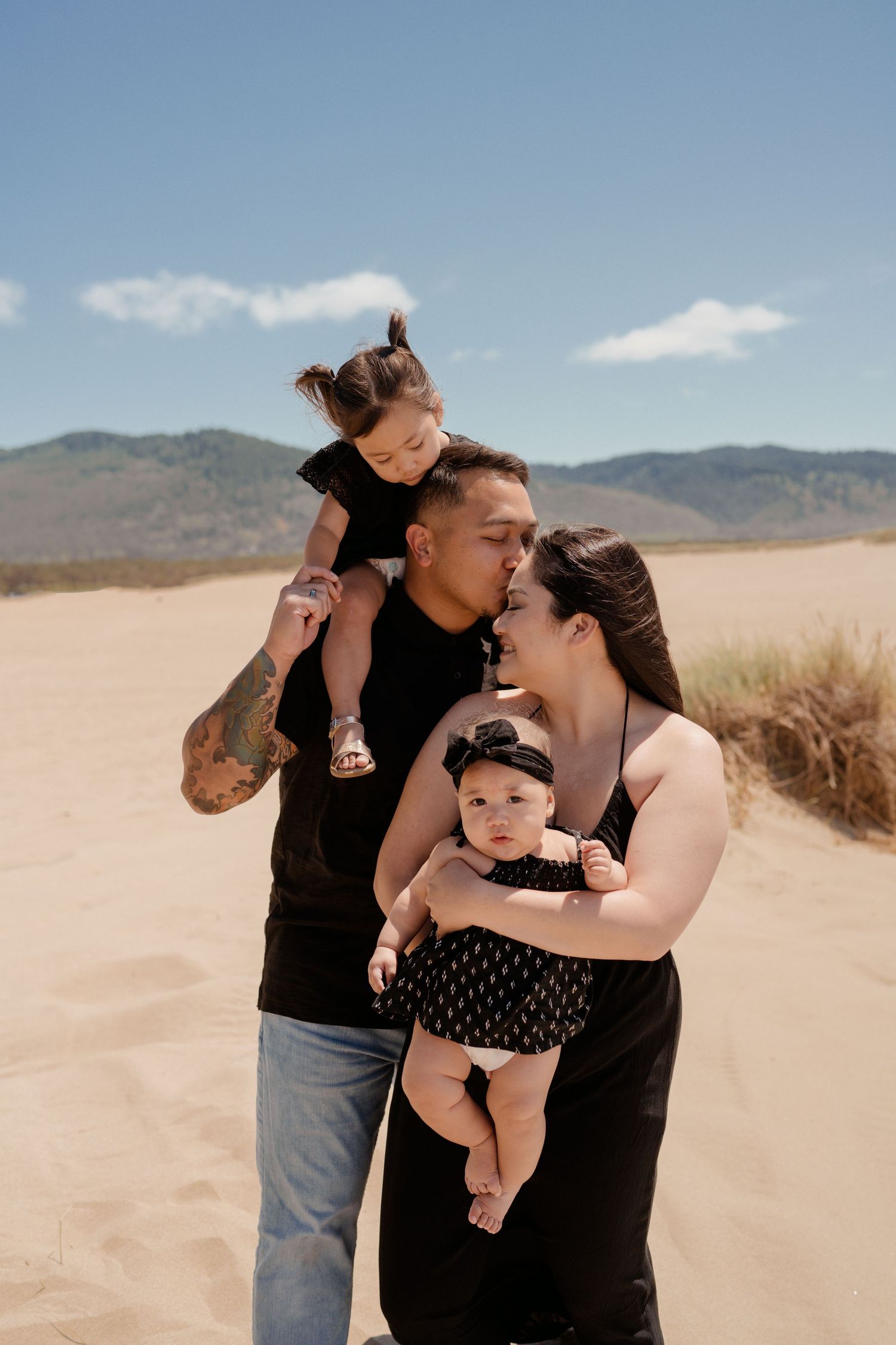 Family embracing on sandy desert terrain with mountains in background.