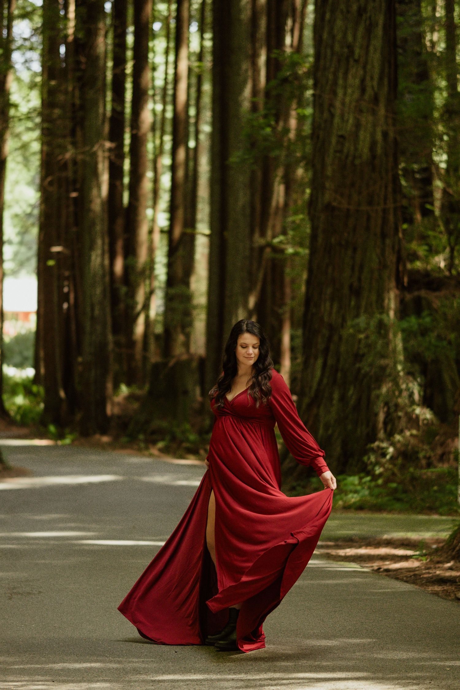 A flowing red dress twirls gracefully on a forest path lined with towering trees.