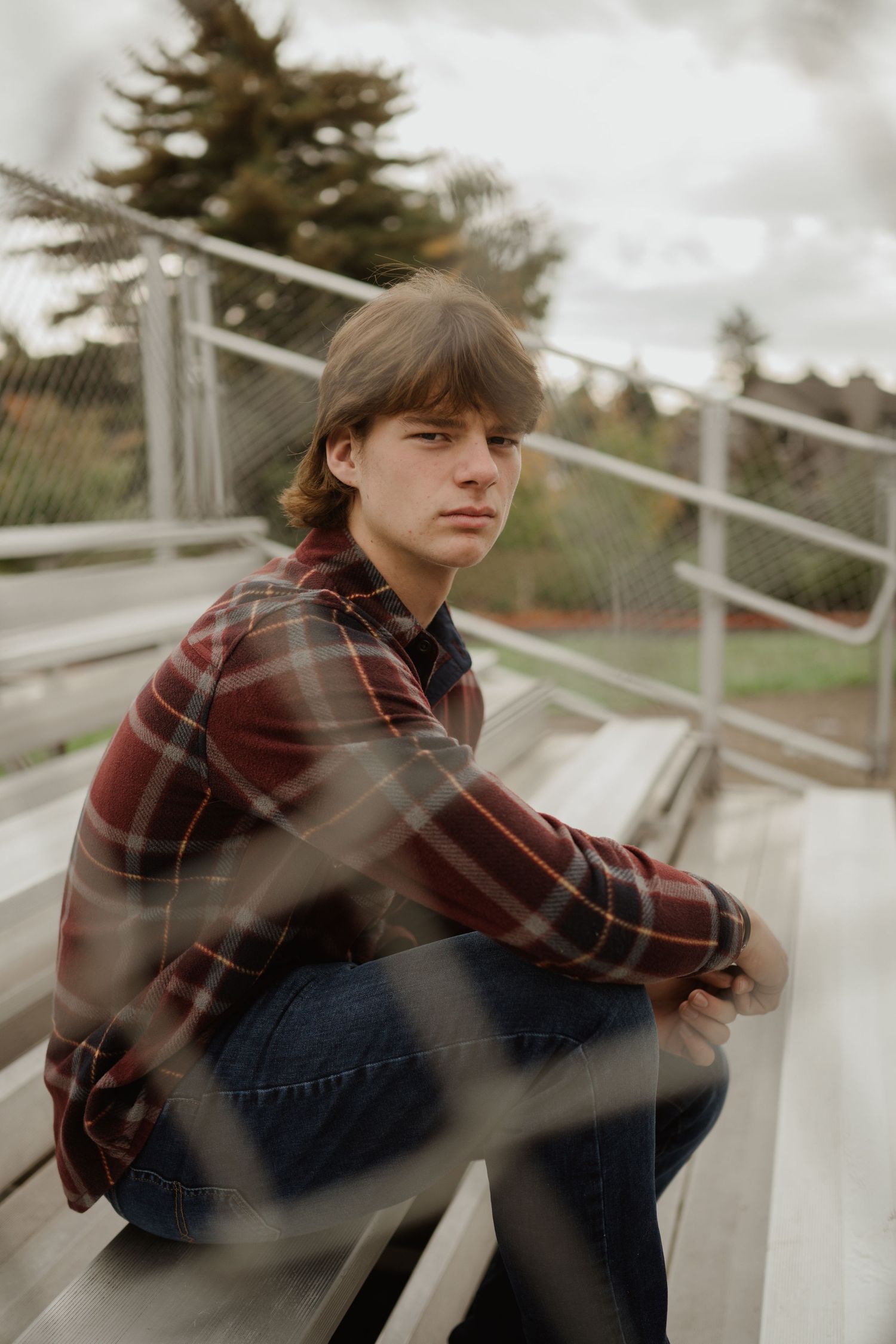 Person in plaid shirt sits on metal bleachers at sports field.