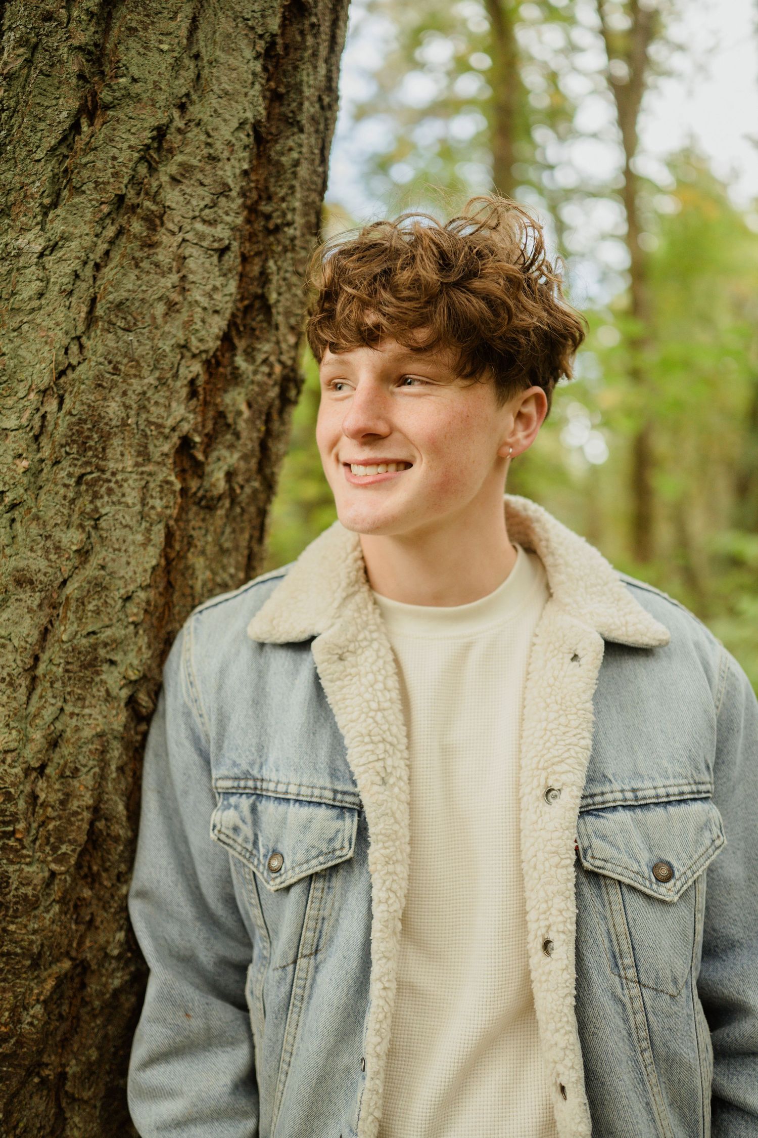 A casual outdoor portrait against a tree trunk wearing a sherpa-lined denim jacket.