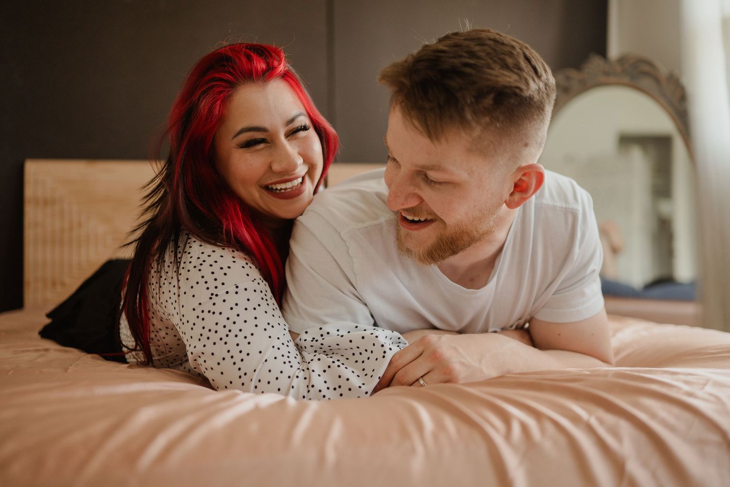A couple sharing a joyful moment while lying on a bed together in casual attire.