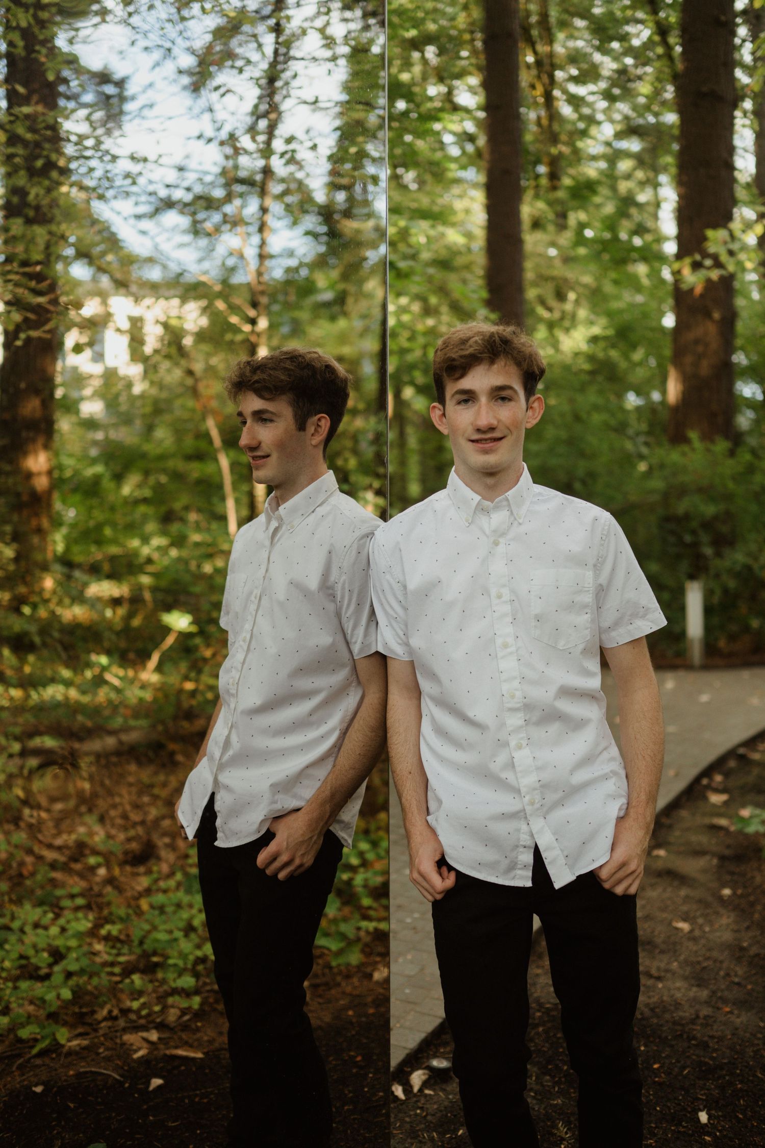 Two figures in matching white button-up shirts pose in wooded setting.