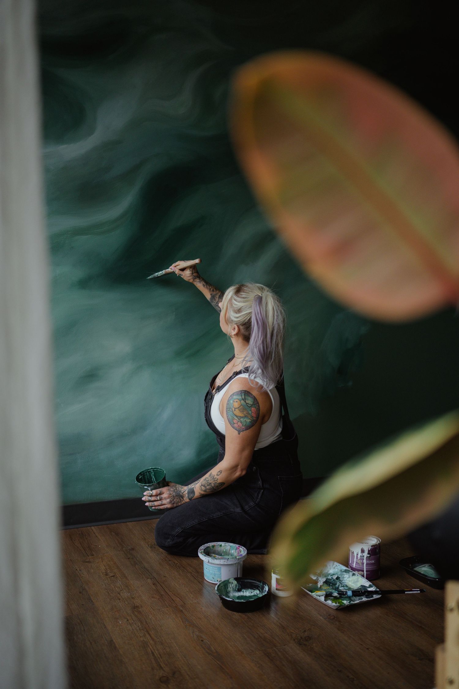 Person with tattoos smoking in dark room with plants in foreground.