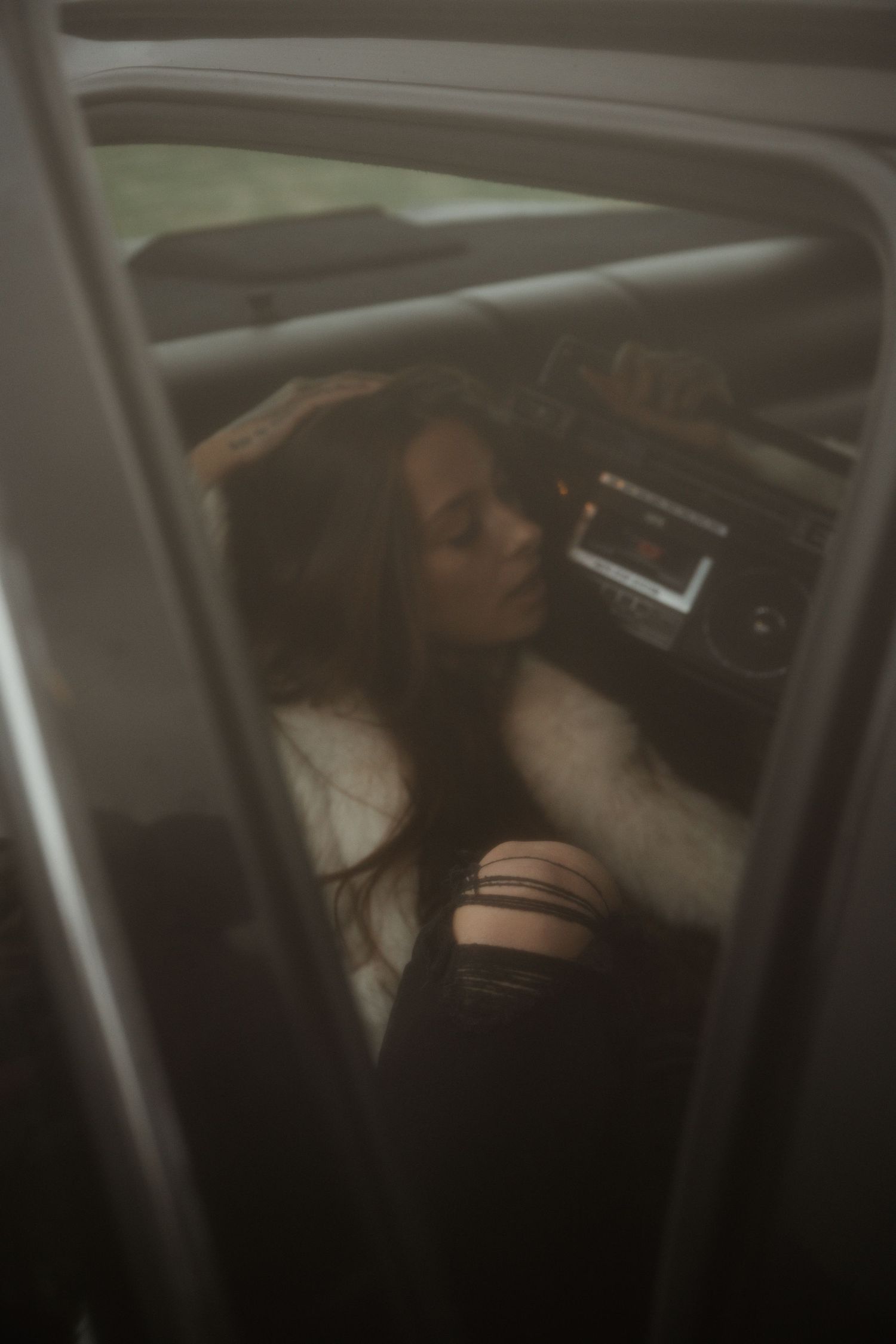 A moody interior car photo of a person resting against the dashboard in dim lighting with a vintage aesthetic.