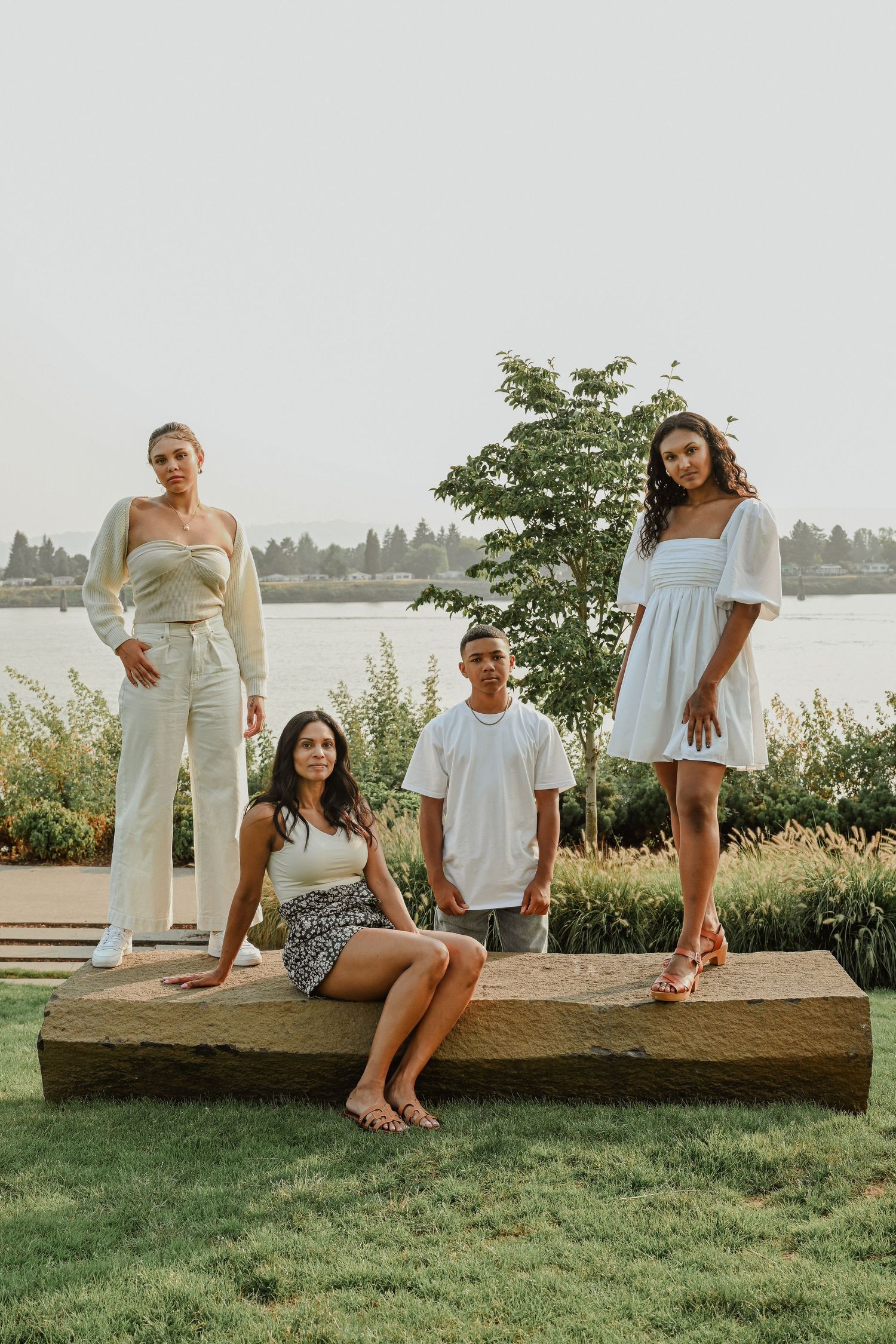 Four people in stylish white outfits posing together on wooden bench by waterfront.