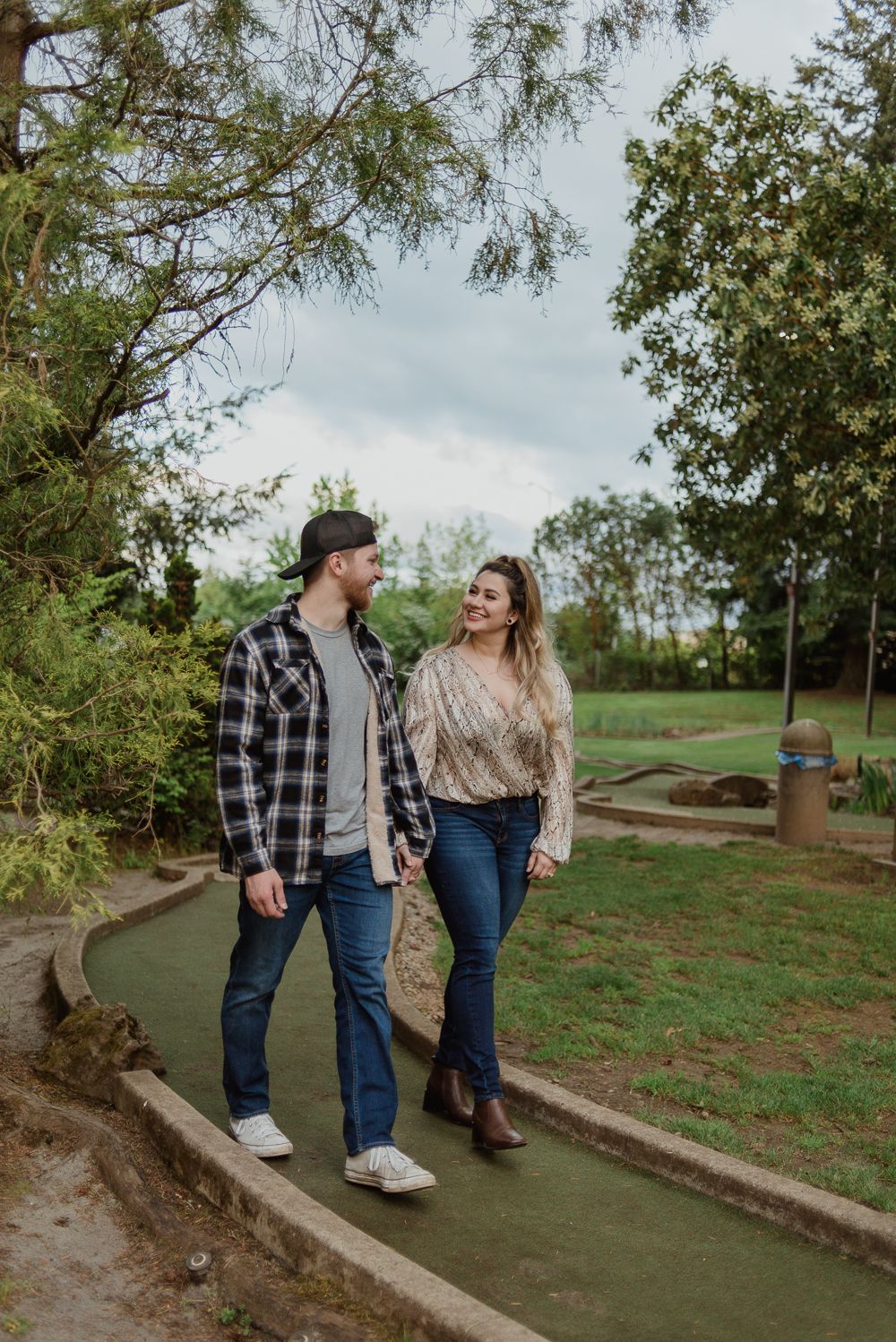 A couple walking together on a mini golf course path surrounded by autumn trees.