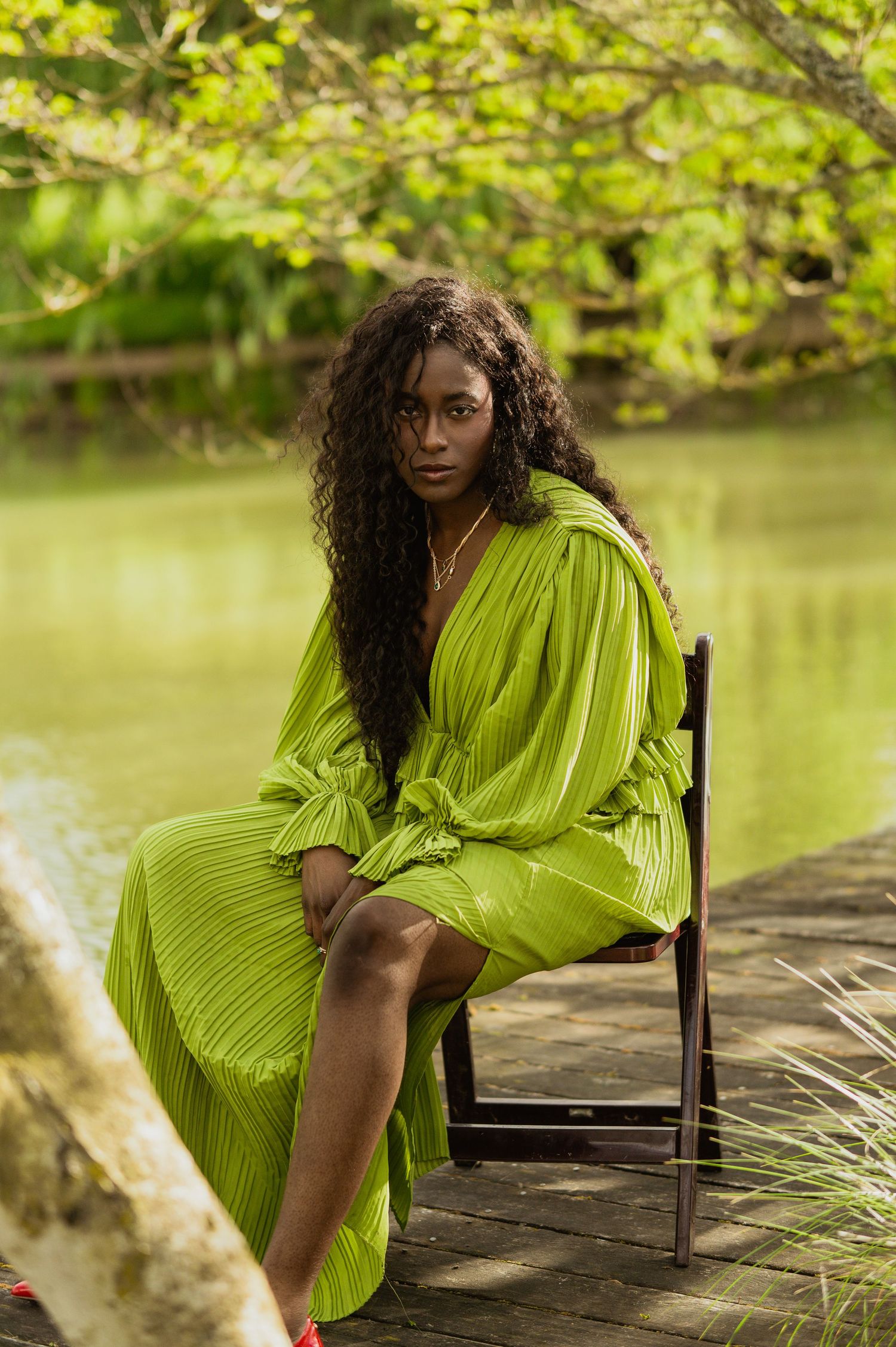 A lime green pleated dress contrasts beautifully with a tranquil pond setting on a wooden dock.