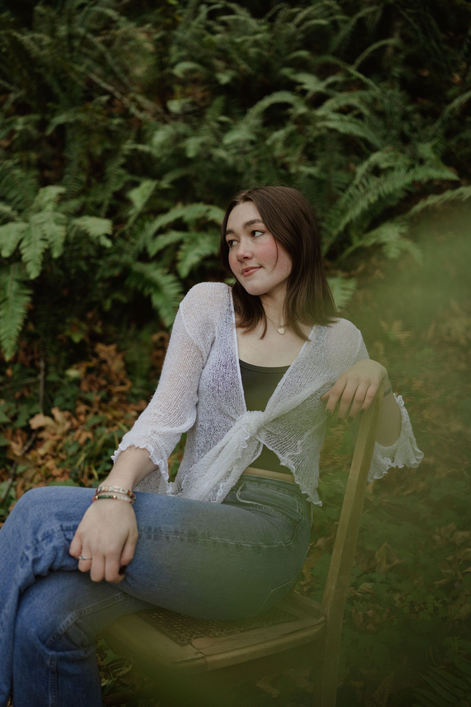 Artistic outdoor portrait against green foliage featuring white lace cardigan and casual denim.