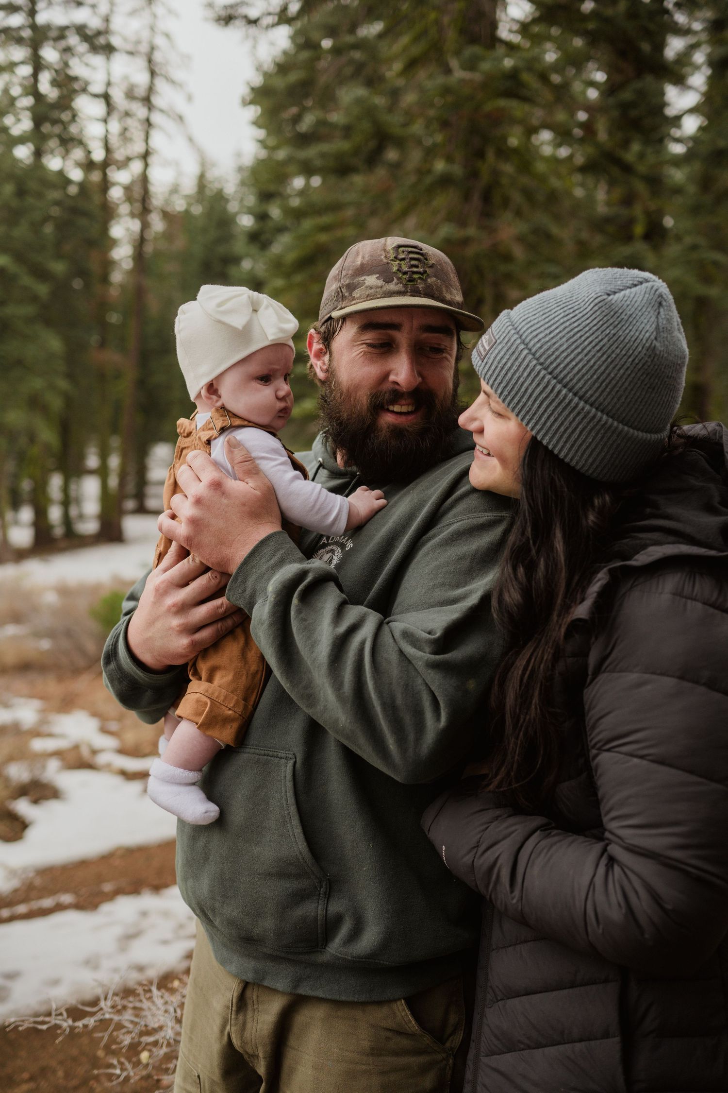 Intimate family portrait in winter forest with casual outdoor clothing and natural lighting.