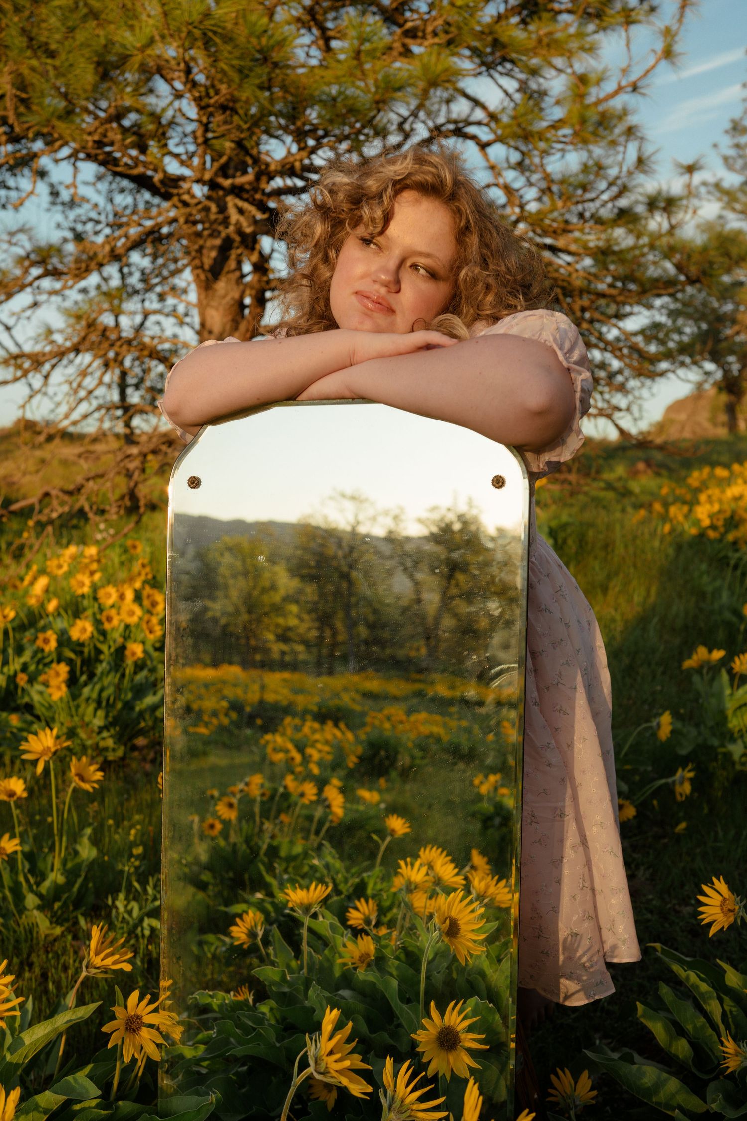 Dreamy portrait leaning on mirror surrounded by yellow wildflowers at golden hour.