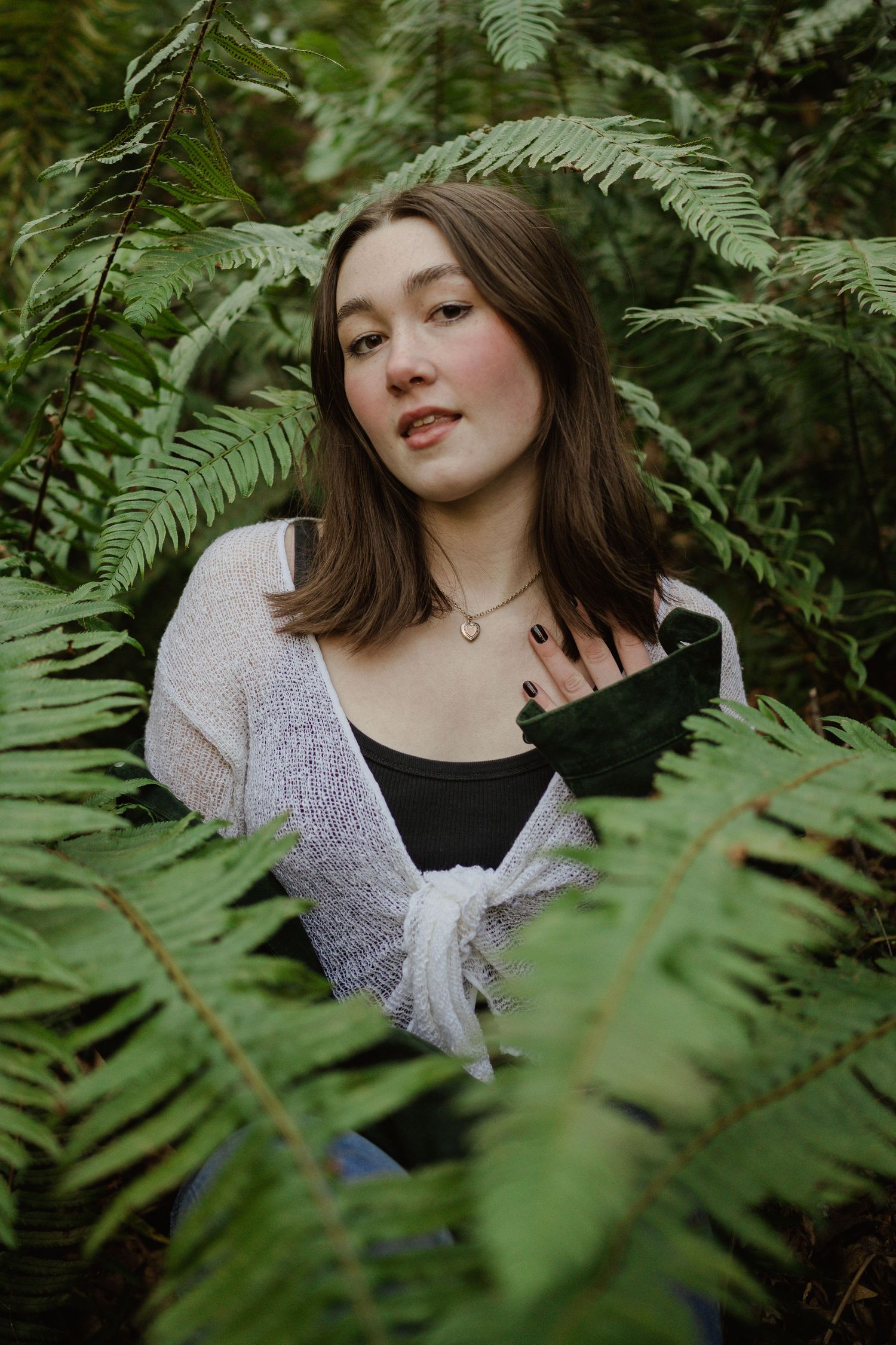 Portrait through fern leaves showing delicate white cardigan and natural woodland background.