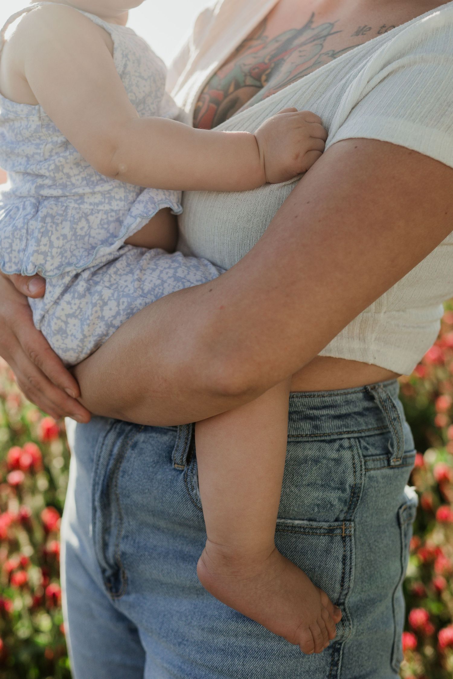 Close up of parents holding a baby wearing a blue dress outdoors.