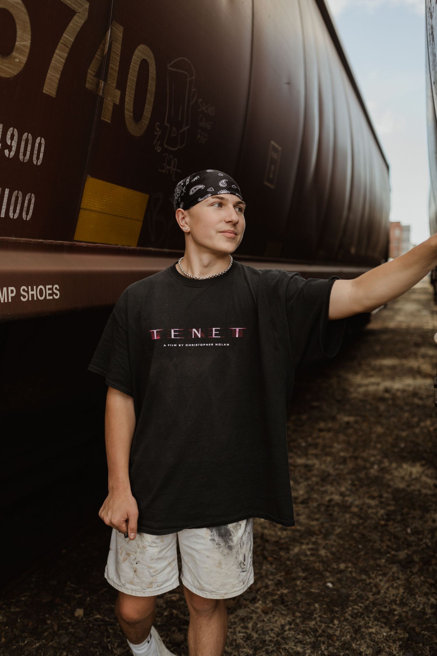 Person in TENET shirt standing beside train car in moody lighting.