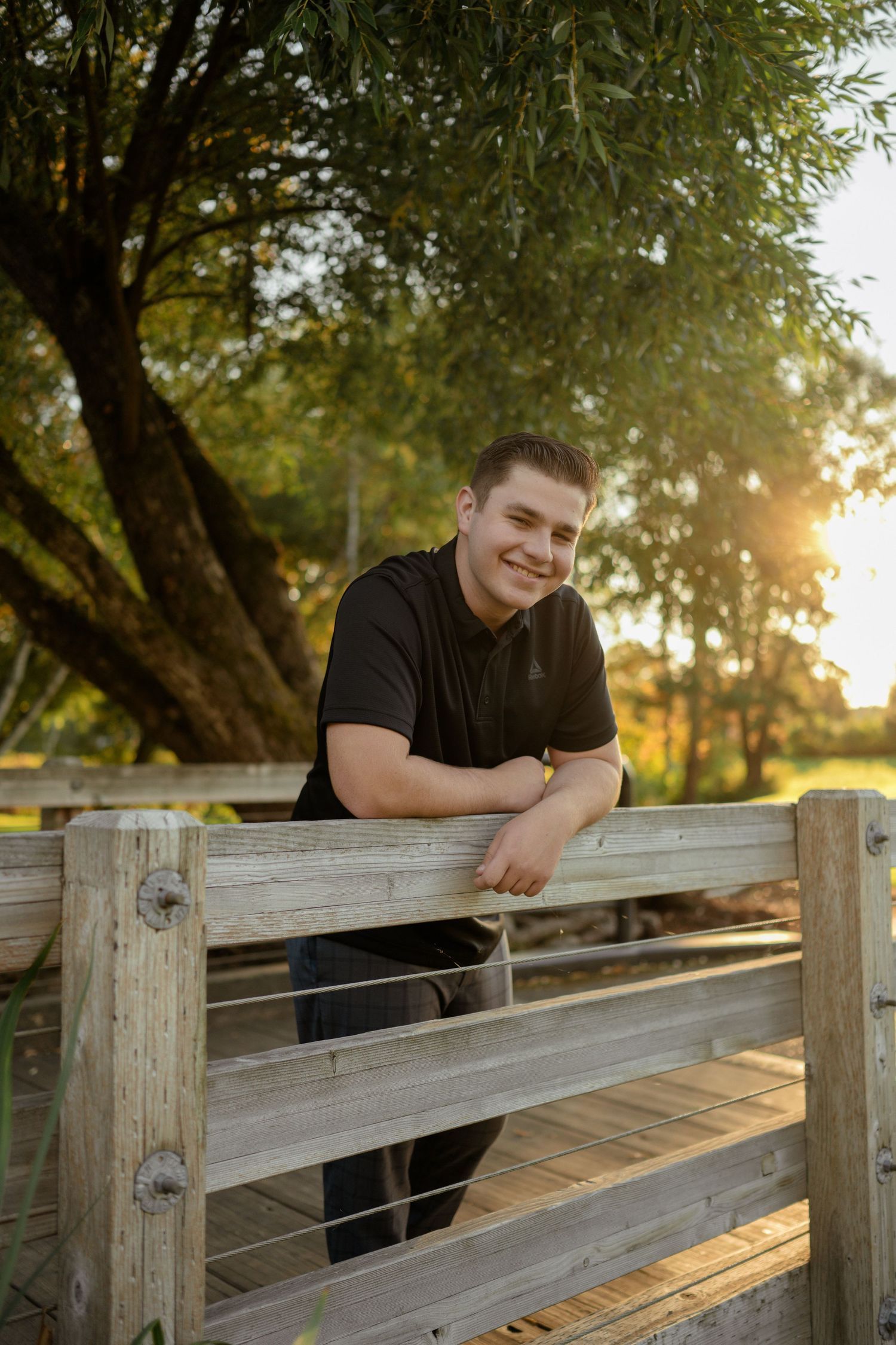 Person leaning on wooden fence railing during golden hour sunset.