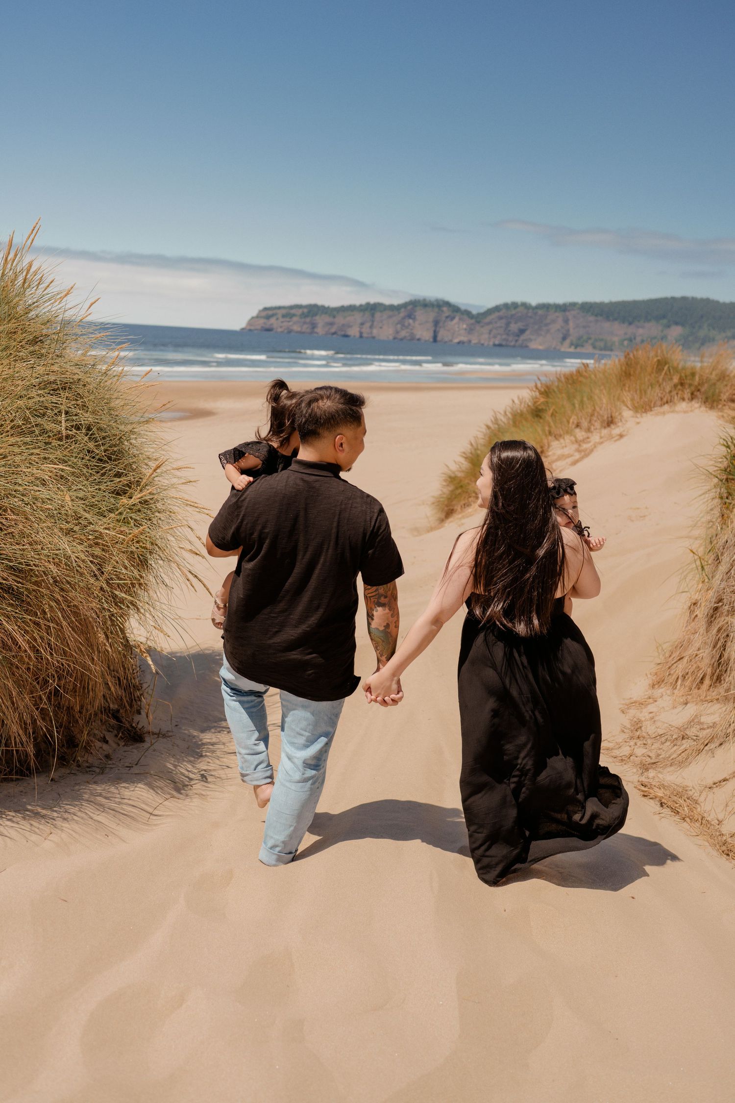 Two people holding hands while walking on sandy beach path with coastal cliffs in background.