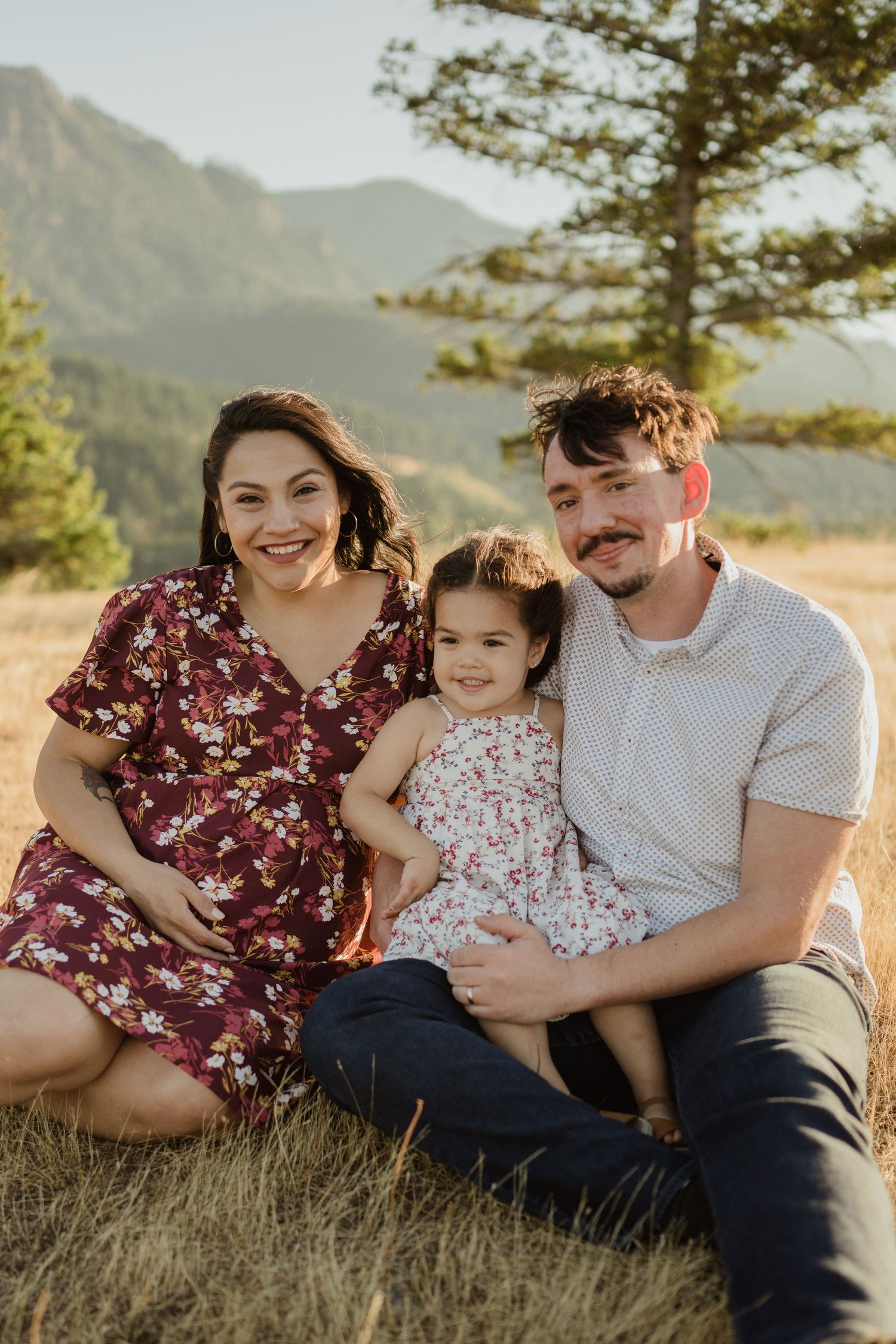 Family of three sitting together in mountain meadow at sunset.