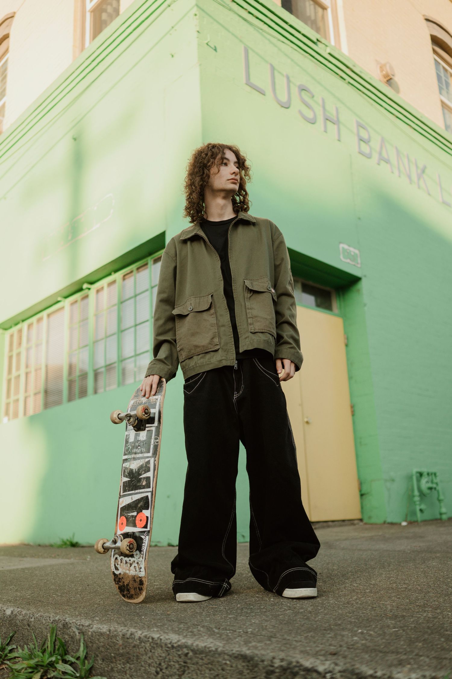 A skateboarder in wide-leg pants poses outside a mint green building.